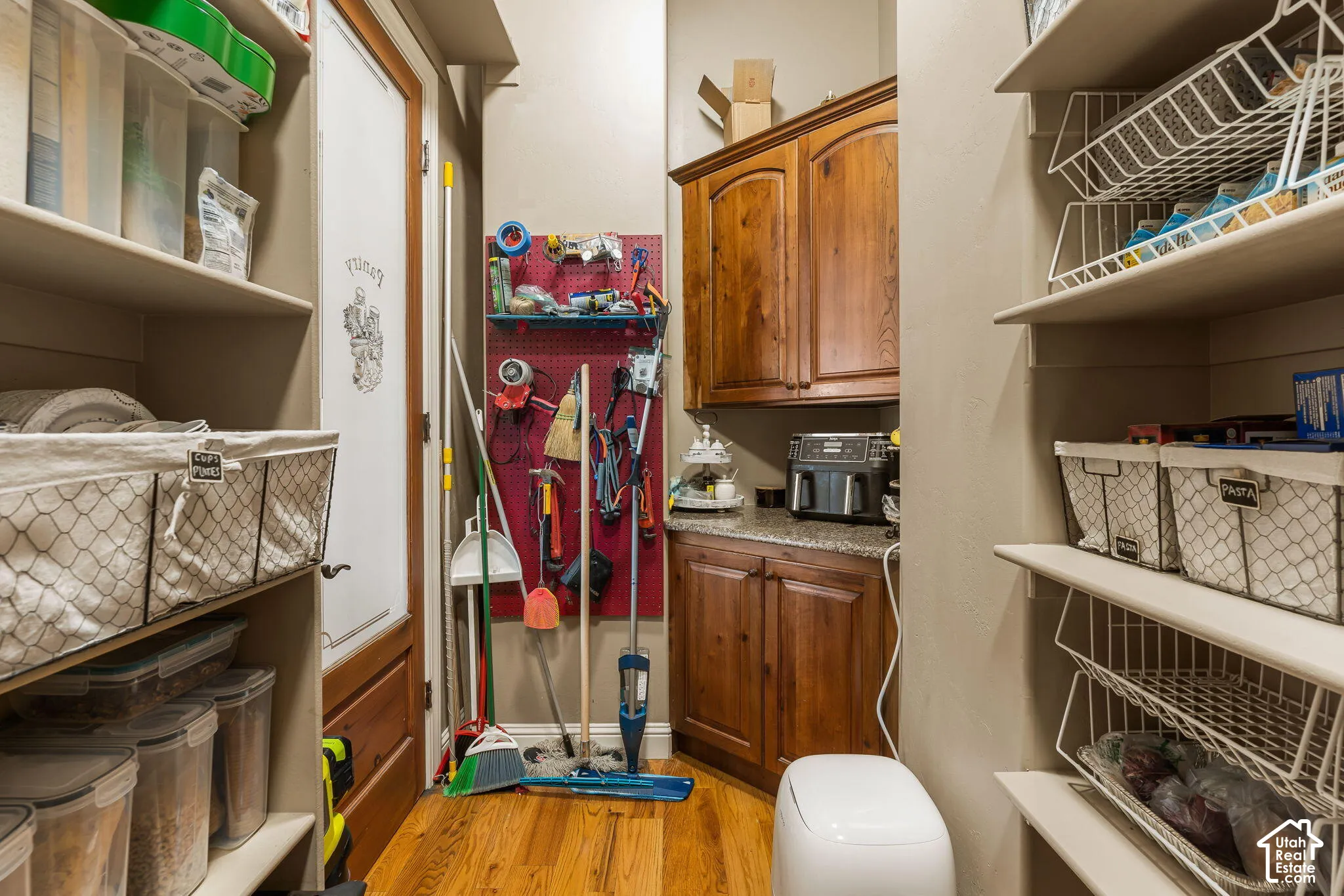 Built-in shelving, wood-finish flooring, pegboard wall organization, wood cabinetry, and granite-look countertop