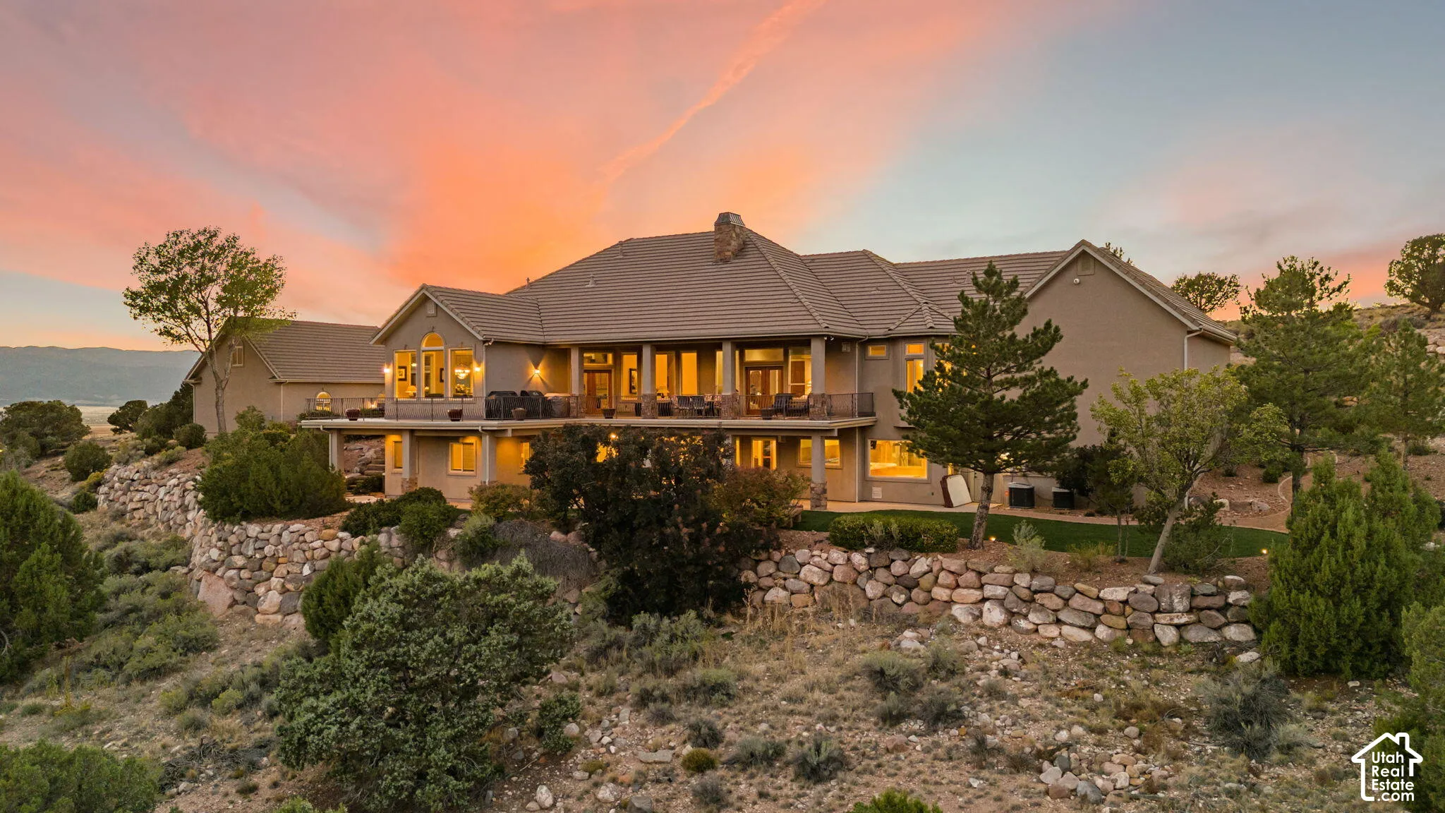 Expansive exterior with multiple levels, featuring a covered balcony, lower patio, and extensive stonework retaining walls
