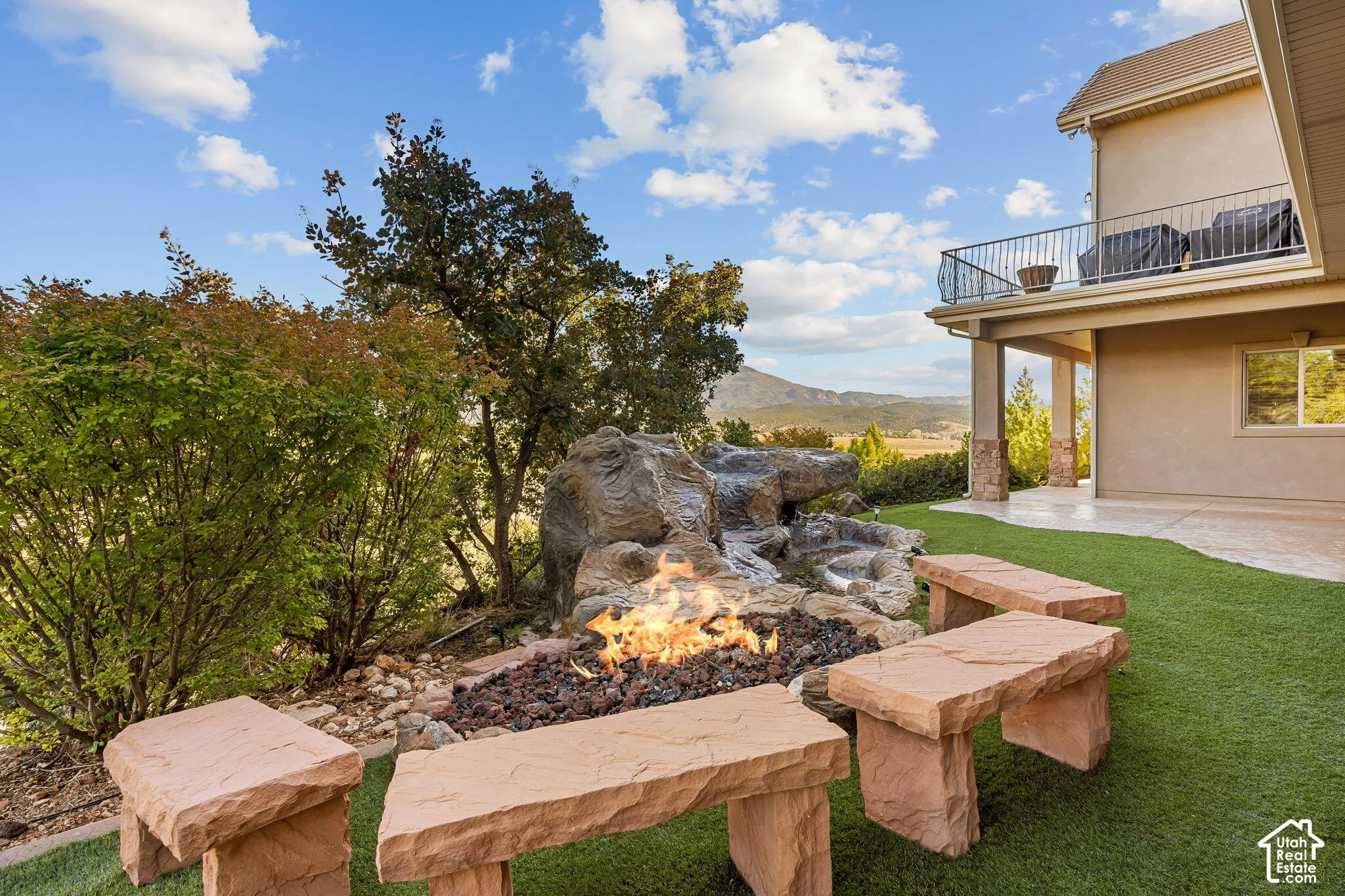 Expansive backyard featuring artificial turf, a rock-detailed water feature, and a built-in fire pit with stone seating