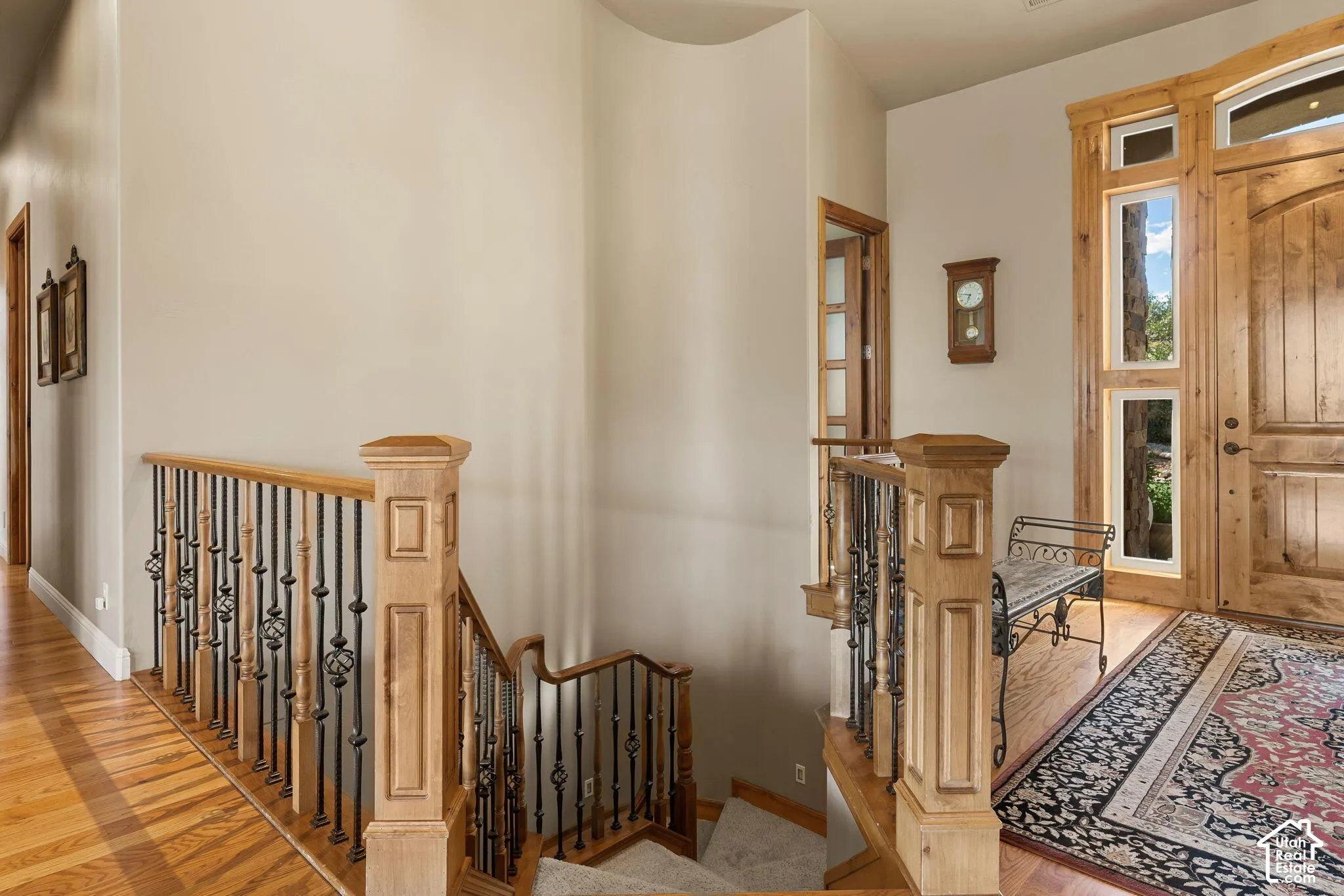 Hardwood flooring, natural wood staircase with wrought iron balusters, natural wood entry door with vertical sidelights, and a curved wall detail