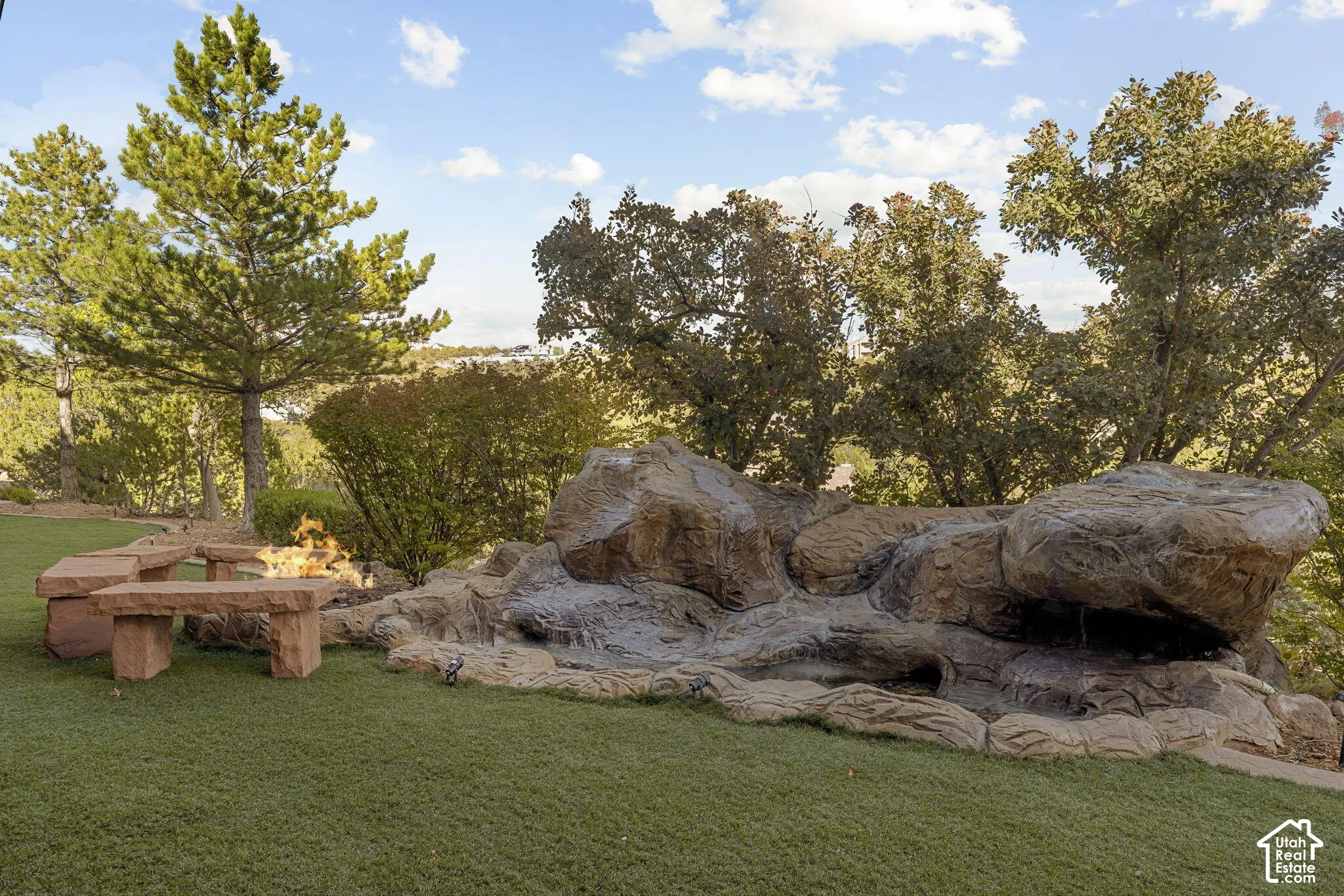 Expansive artificial turf lawn with a rock water feature, stone fire pit, and stone benches