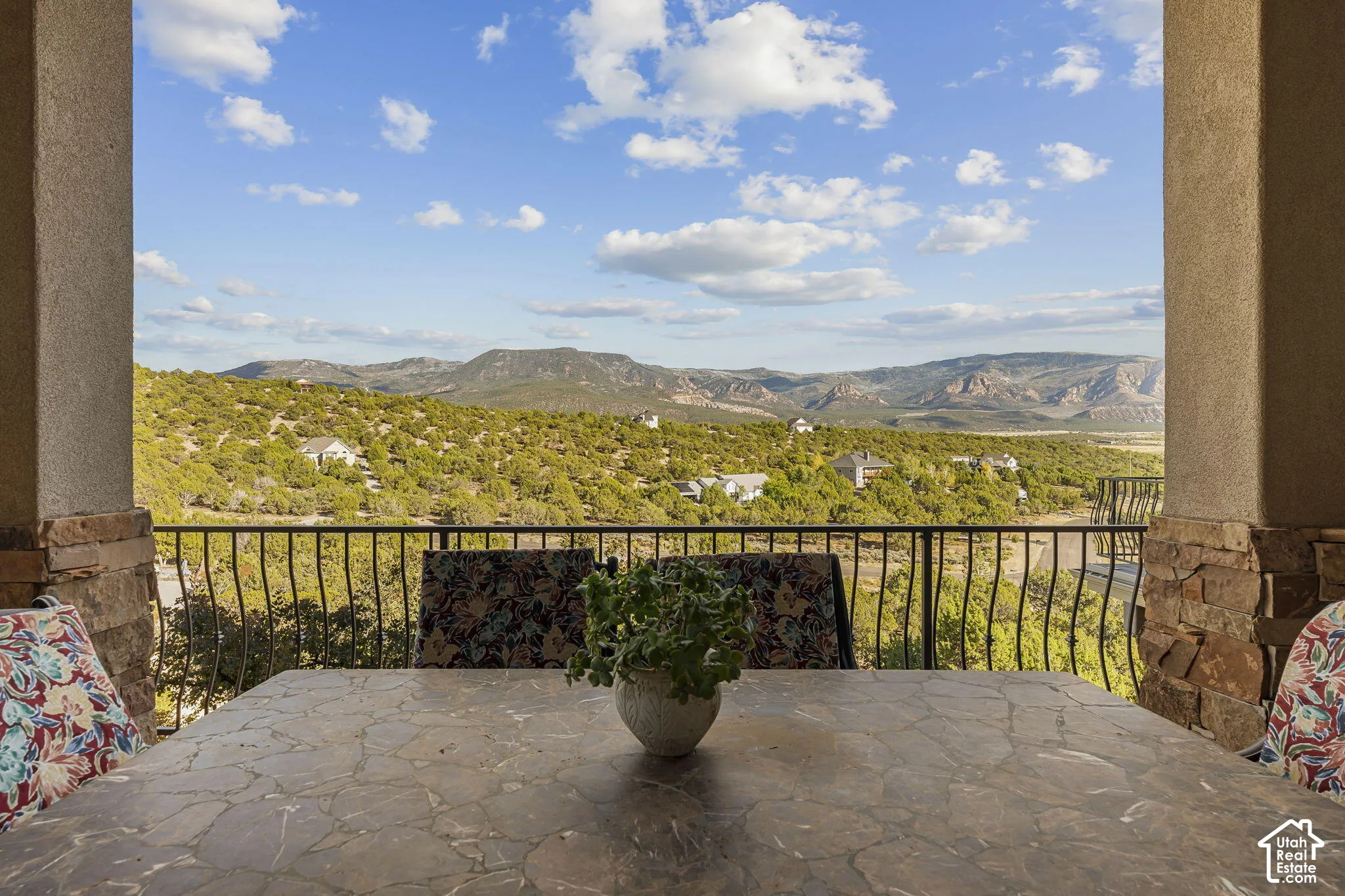 Covered outdoor patio with stone-clad columns, wrought iron railing, and stone-finish flooring