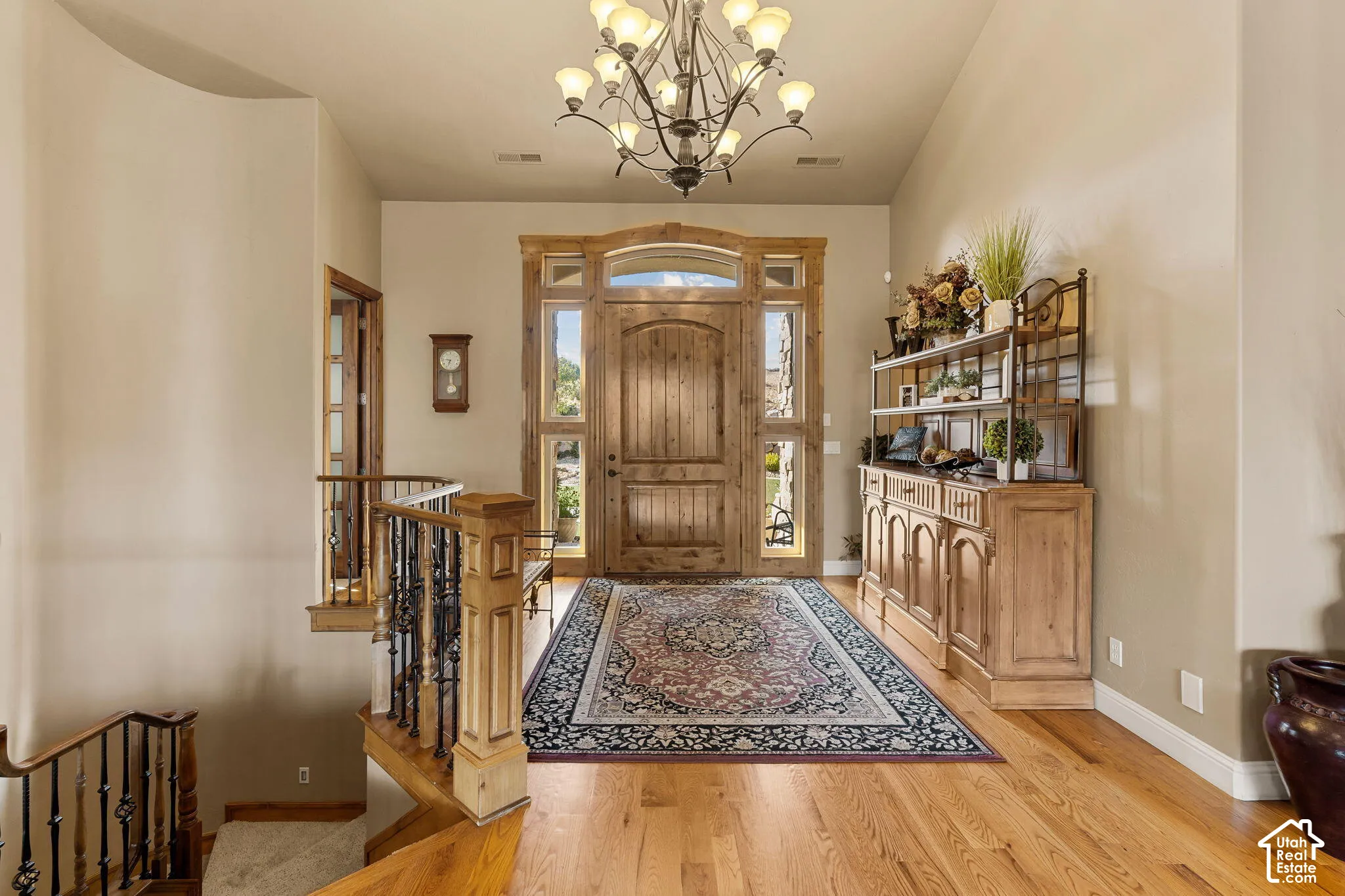 Hardwood flooring, wood-paneled entry door with sidelights, decorative iron chandelier, and a wood staircase with wrought iron balusters
