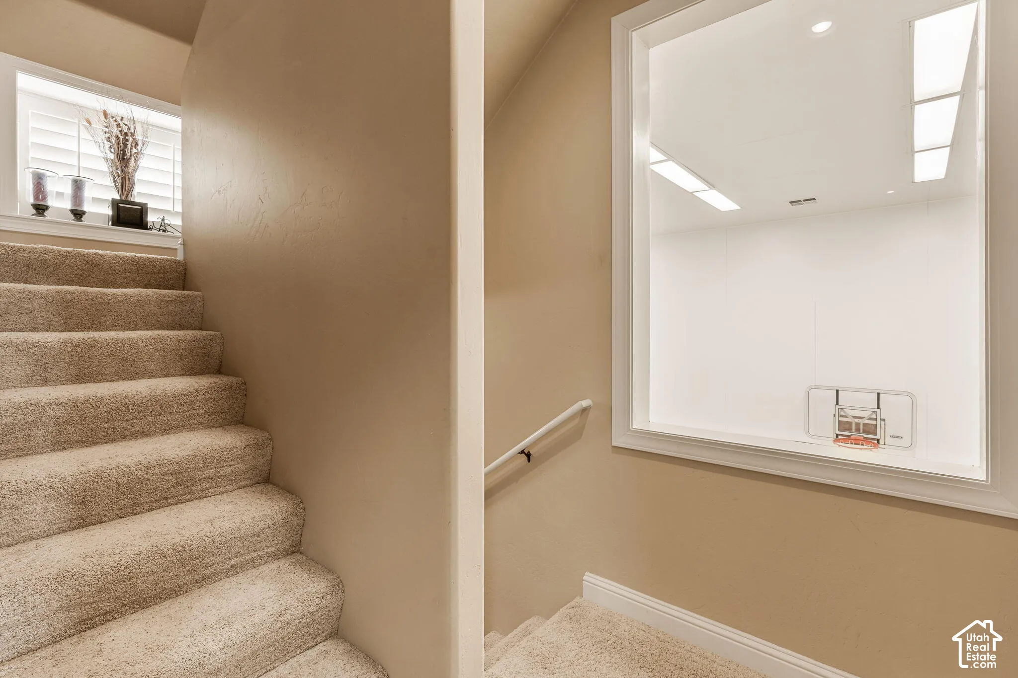 Carpeted staircase with an integrated handrail, textured wall finish, and a window with plantation shutters