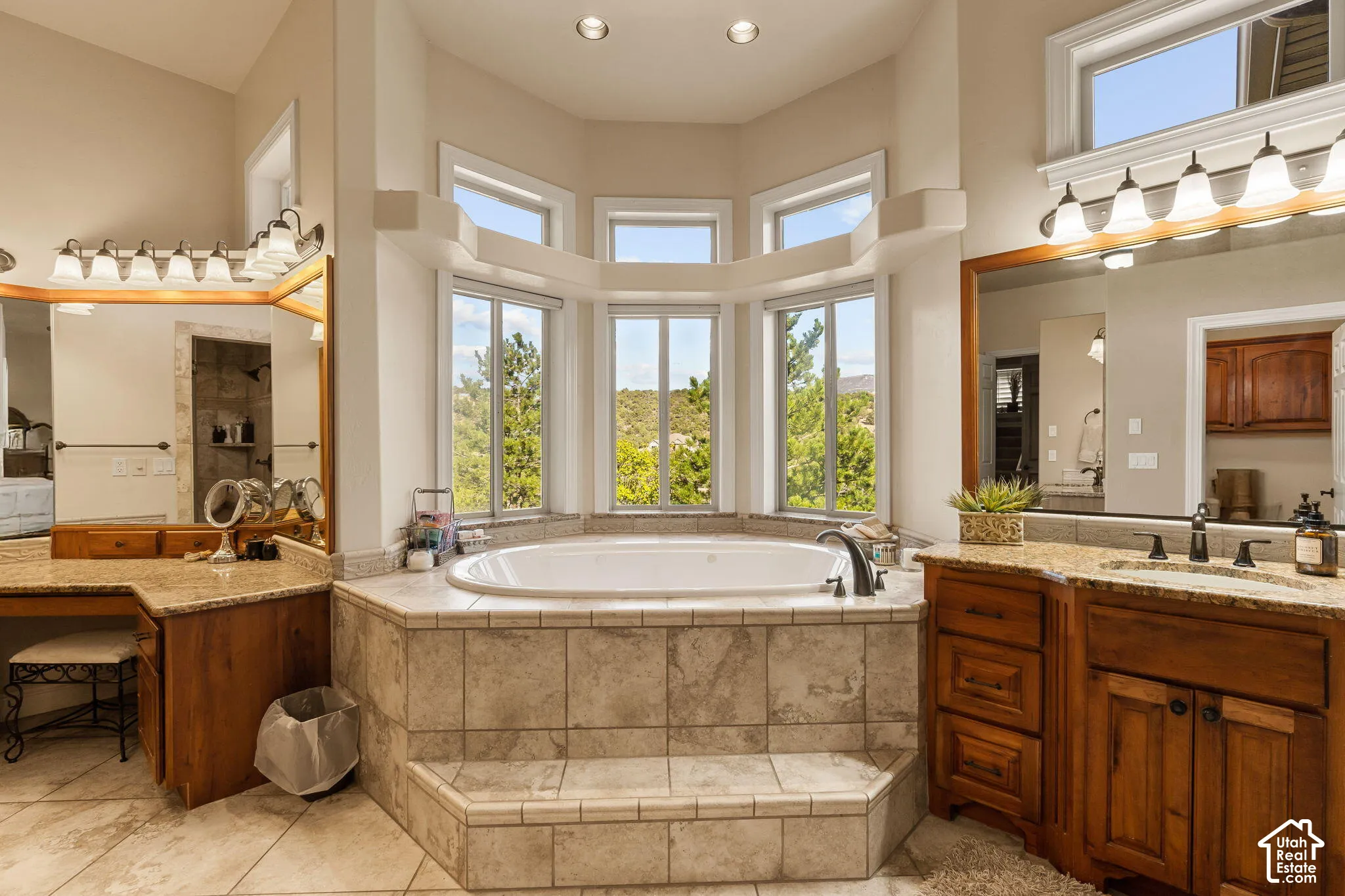 Recessed soaking tub with tiled surround, bay windows, dual wood vanities, granite countertops, and tiled flooring