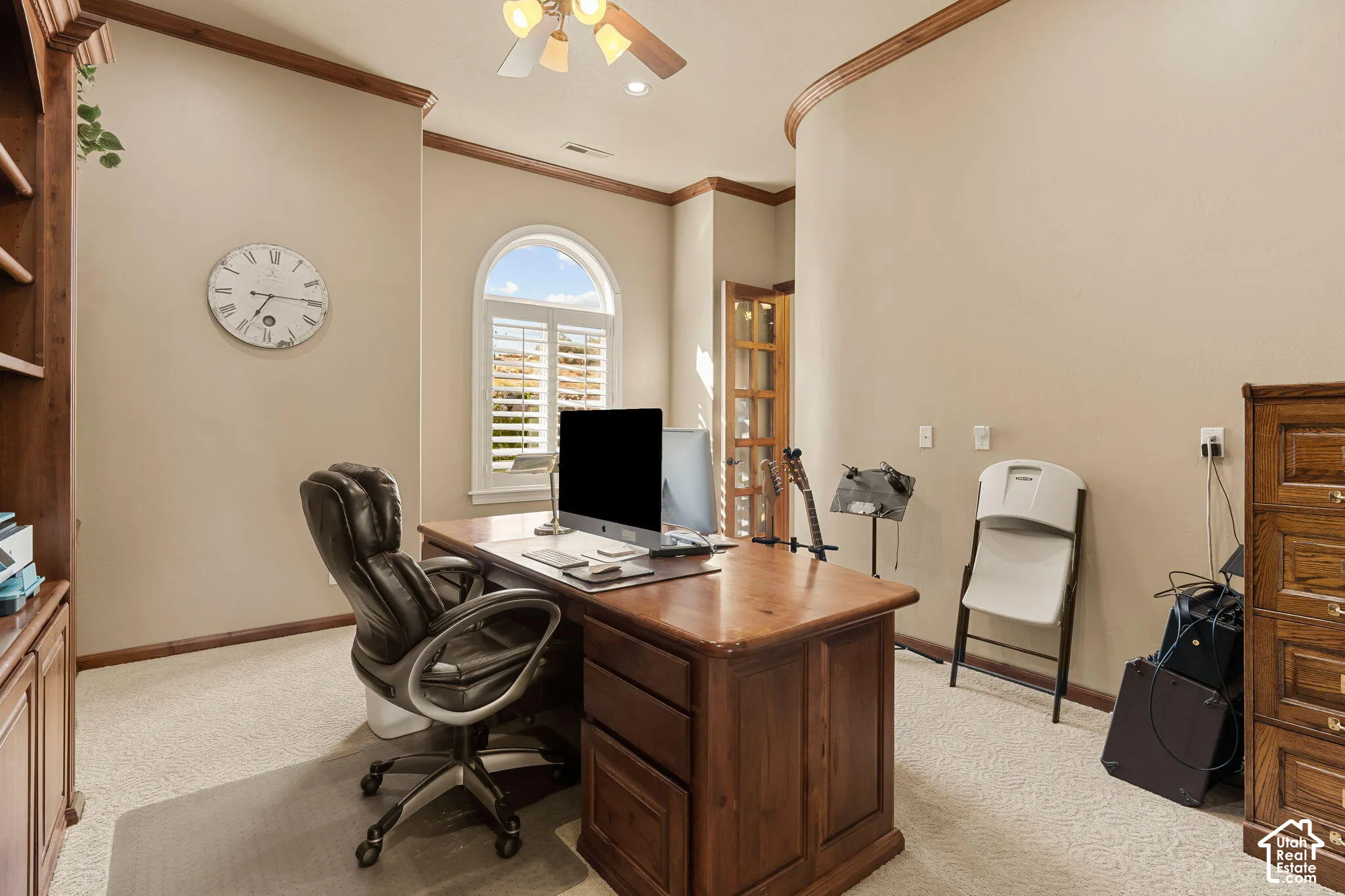 Arched window with plantation shutters, ceiling fan, crown molding, and built-in wood cabinetry
