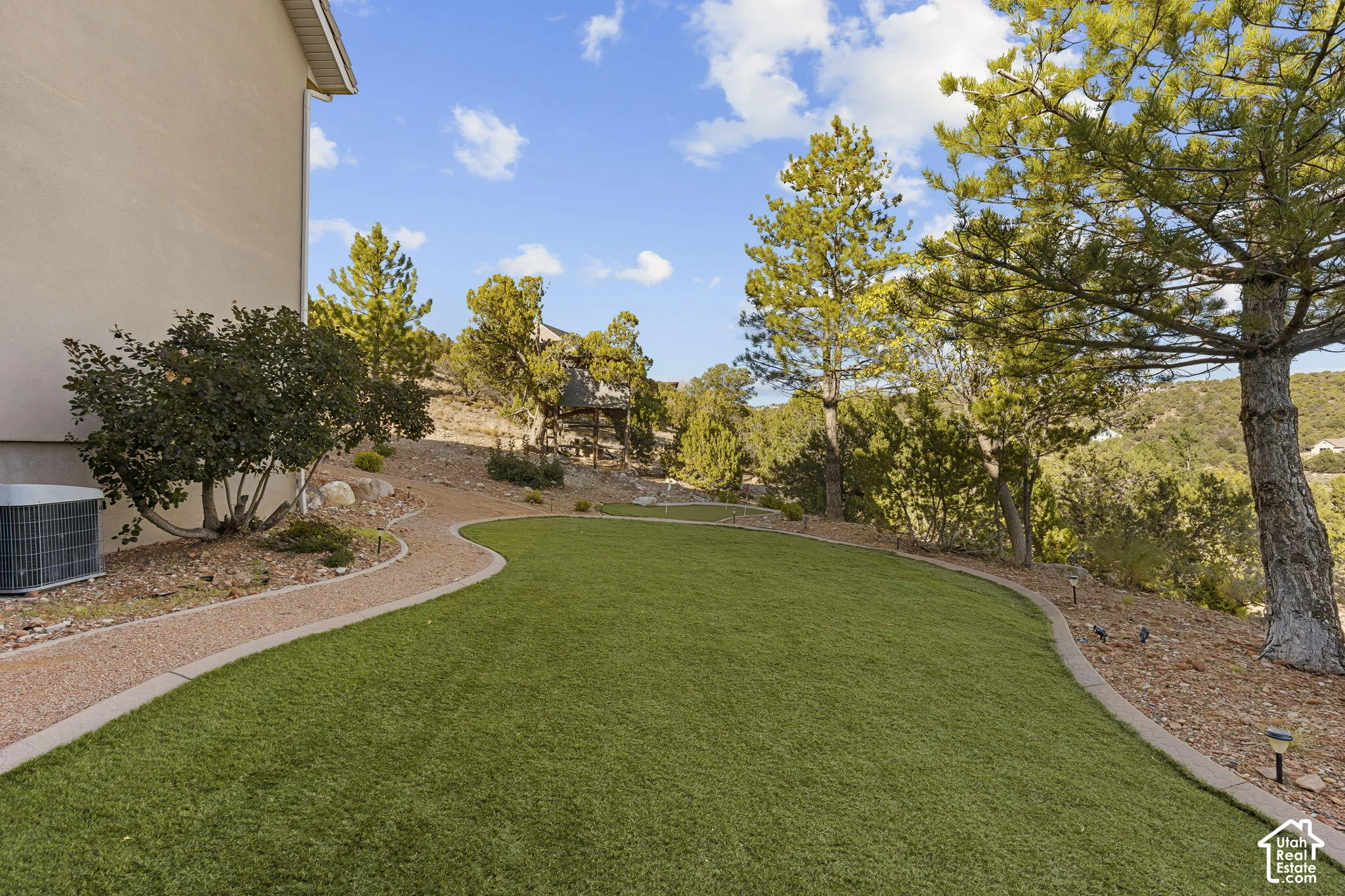 Landscaped yard featuring a manicured artificial turf lawn, a gravel pathway with concrete edging, and mature trees