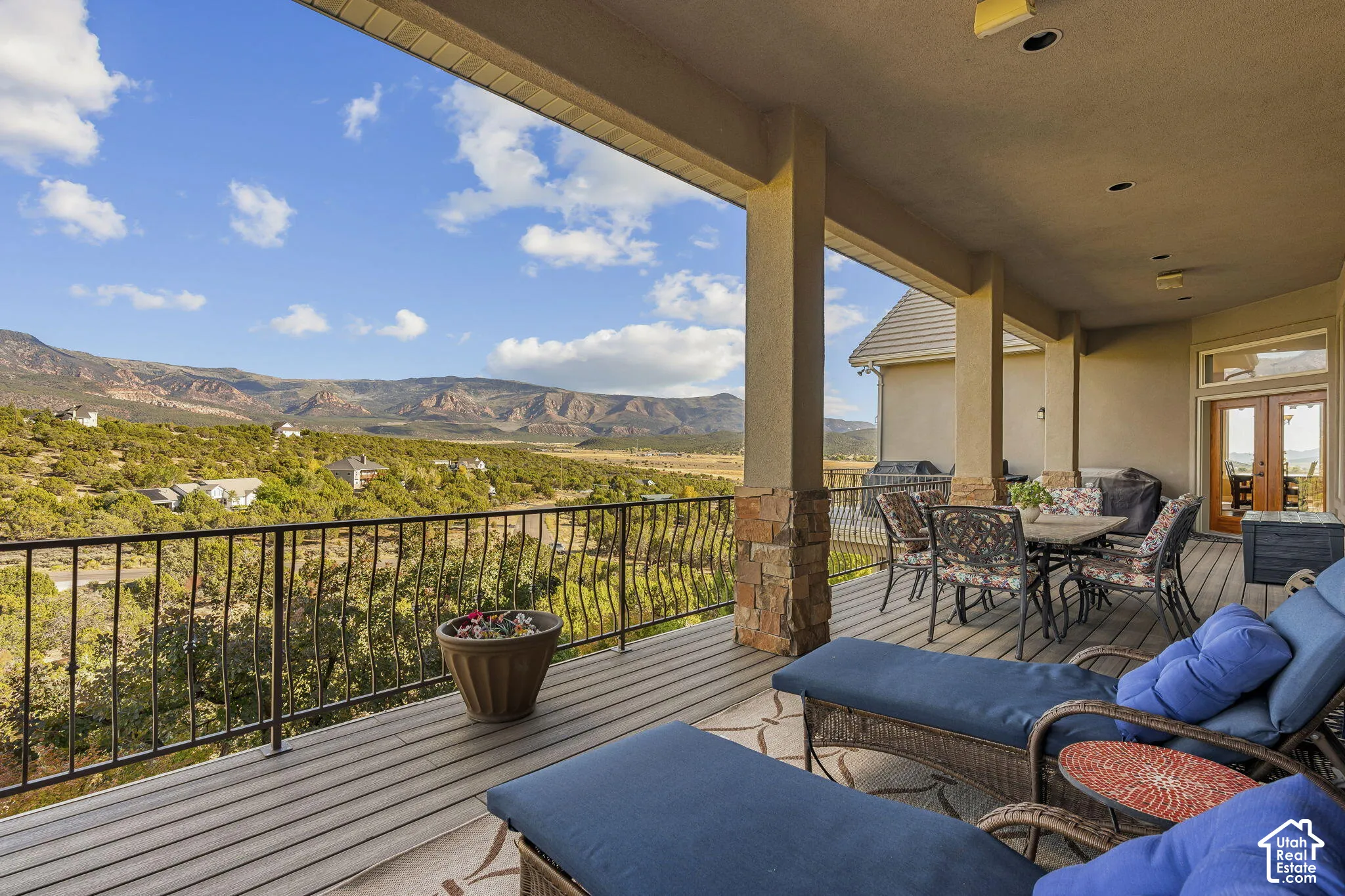 Expansive covered outdoor living space featuring a wood-finish deck, stone-wrapped columns, and a wrought iron railing