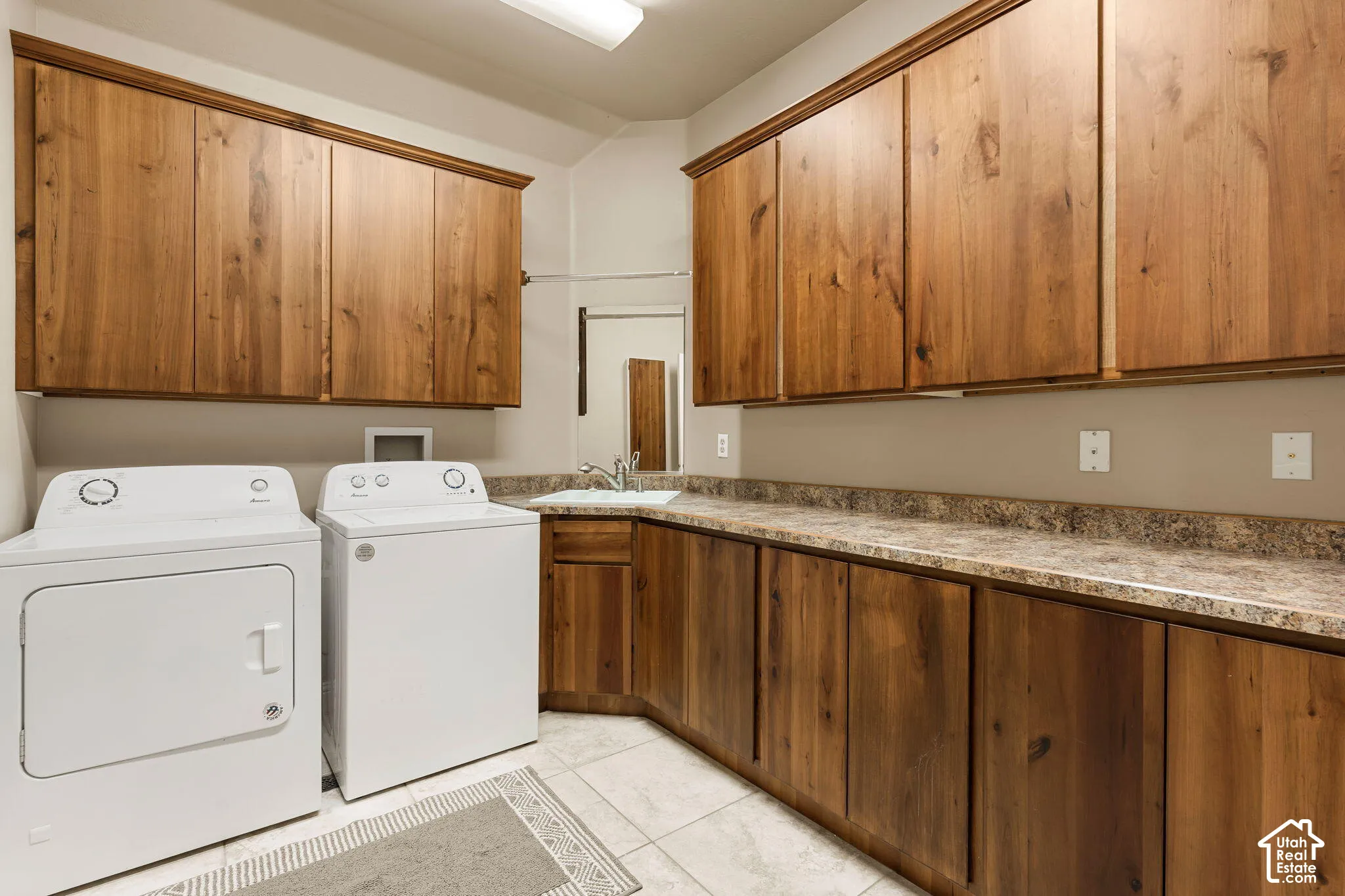 Warm wood-finish cabinetry, neutral countertops, and a utility sink