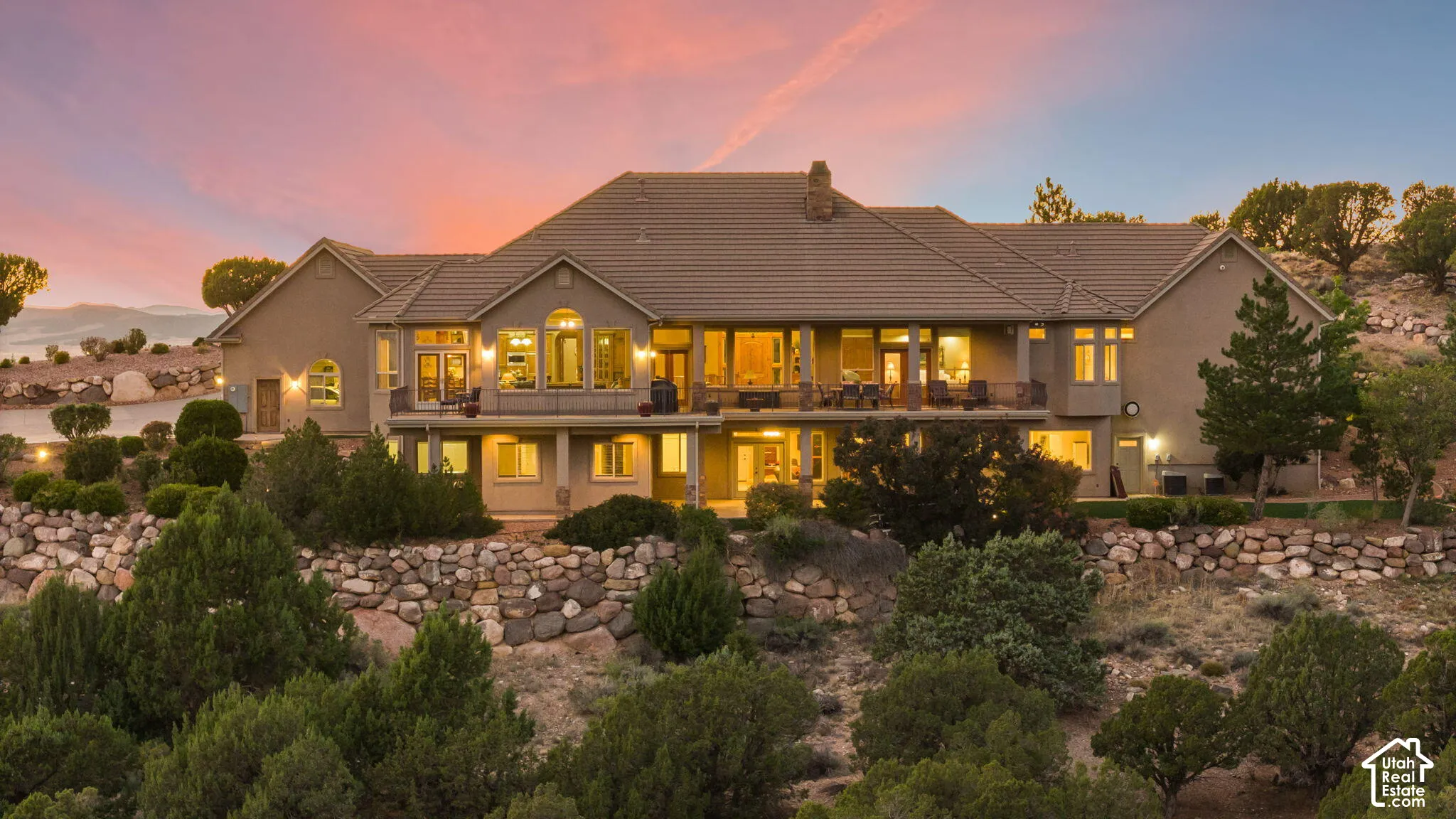 Multi-level residence with extensive window placements, multiple balconies, and a tiled roof, set among natural landscaping with stone retaining walls