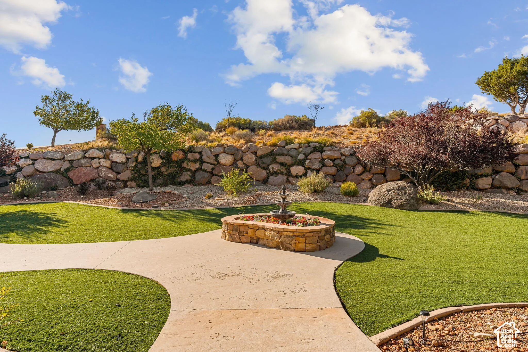 Landscaped rear yard featuring a stone retaining wall, artificial turf, and a stone-clad water feature