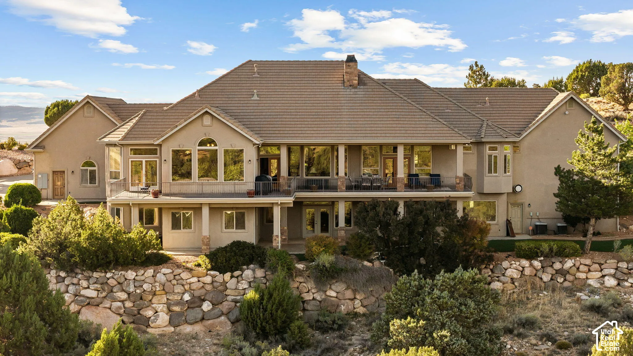Multi-level property with expansive outdoor living spaces, a stone retaining wall, mature landscaping, and a tile roof