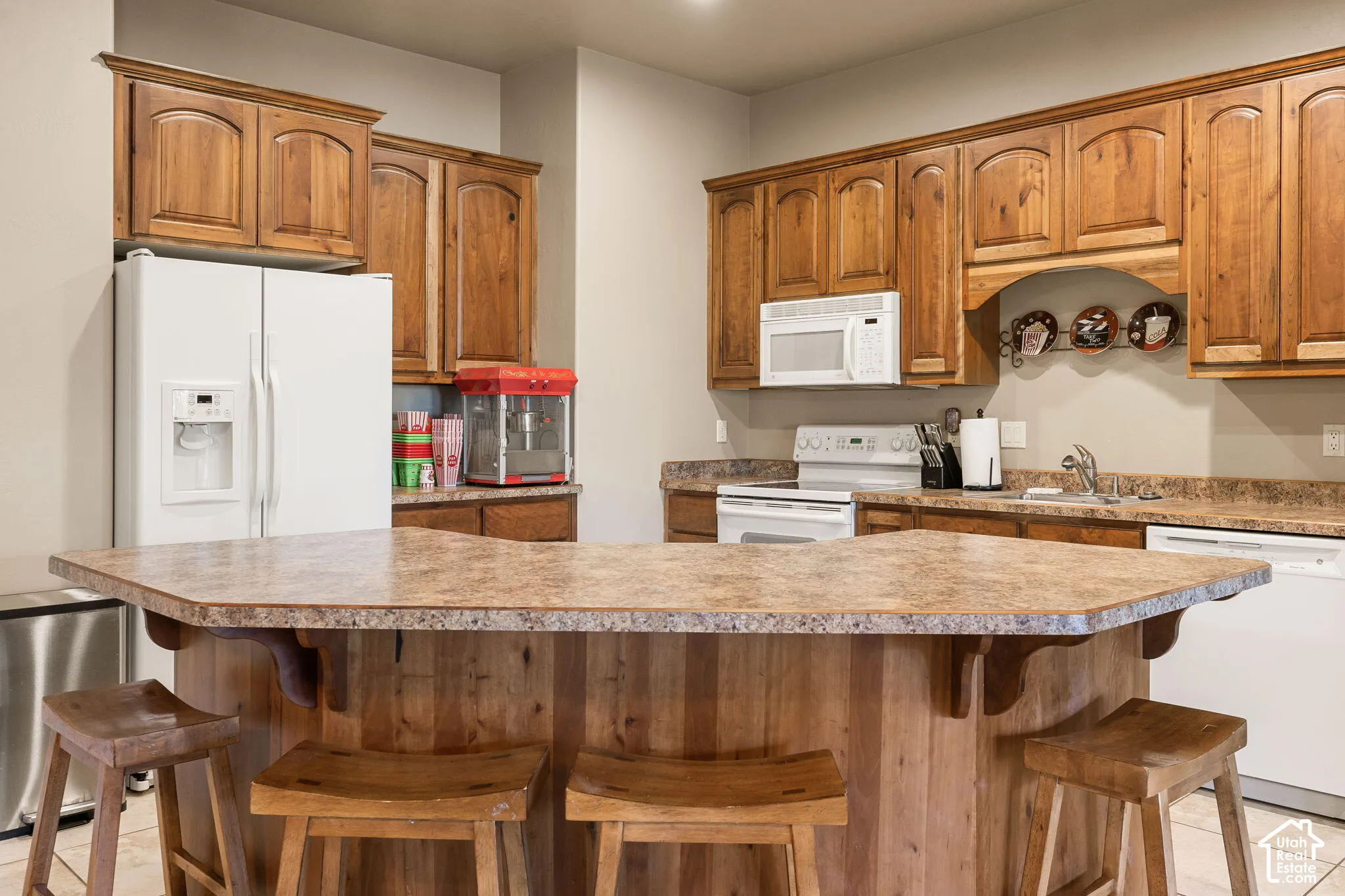Kitchen featuring wood-finish cabinetry, a central island with a multi-faceted countertop, and white appliances