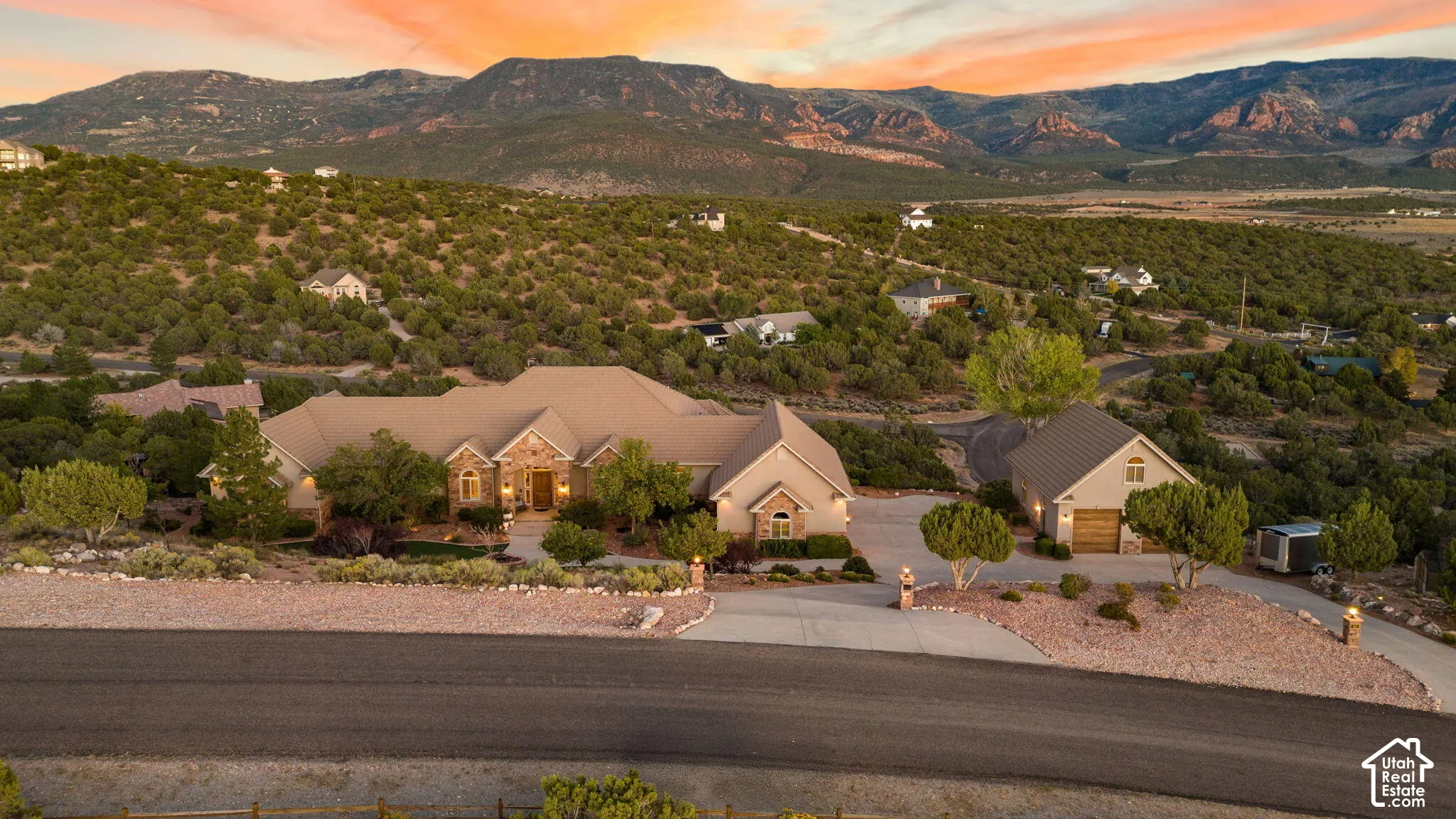 Expansive property featuring a stone and stucco exterior, multiple rooflines, an attached garage, a detached garage, and a long asphalt driveway