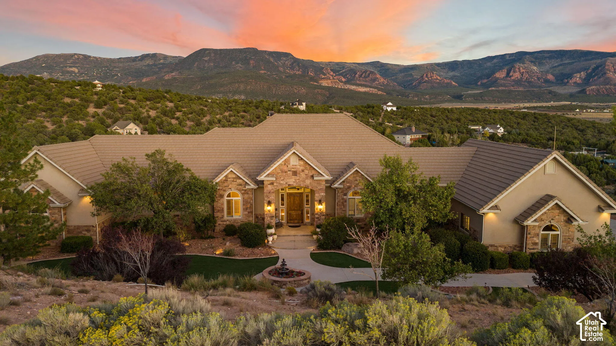 Expansive dwelling featuring a tile roof, stucco and stone exterior, a decorative water feature, and a paved circular drive