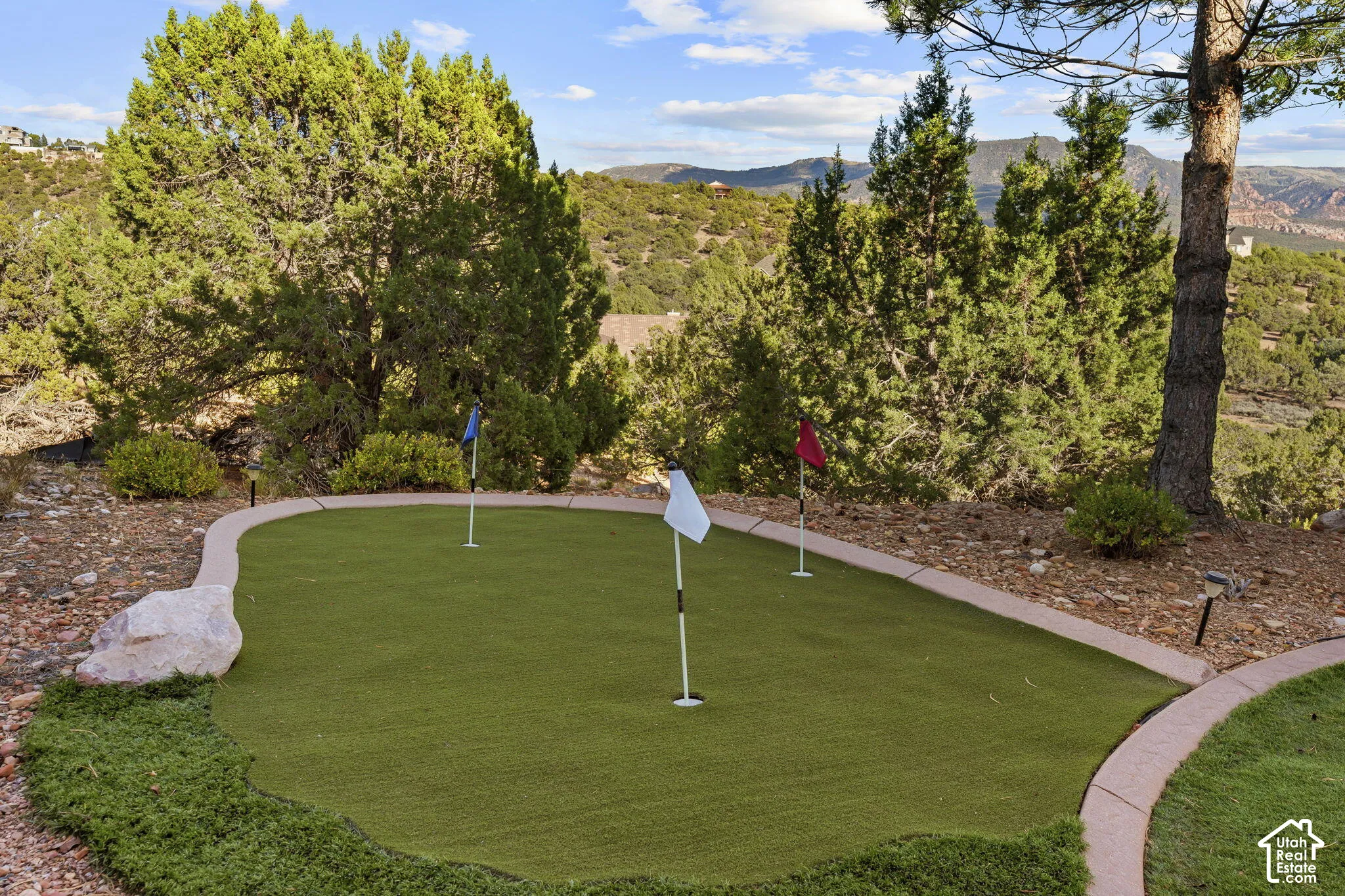 Putting green with multiple holes, defined by a hardscaped border and surrounding natural landscaping