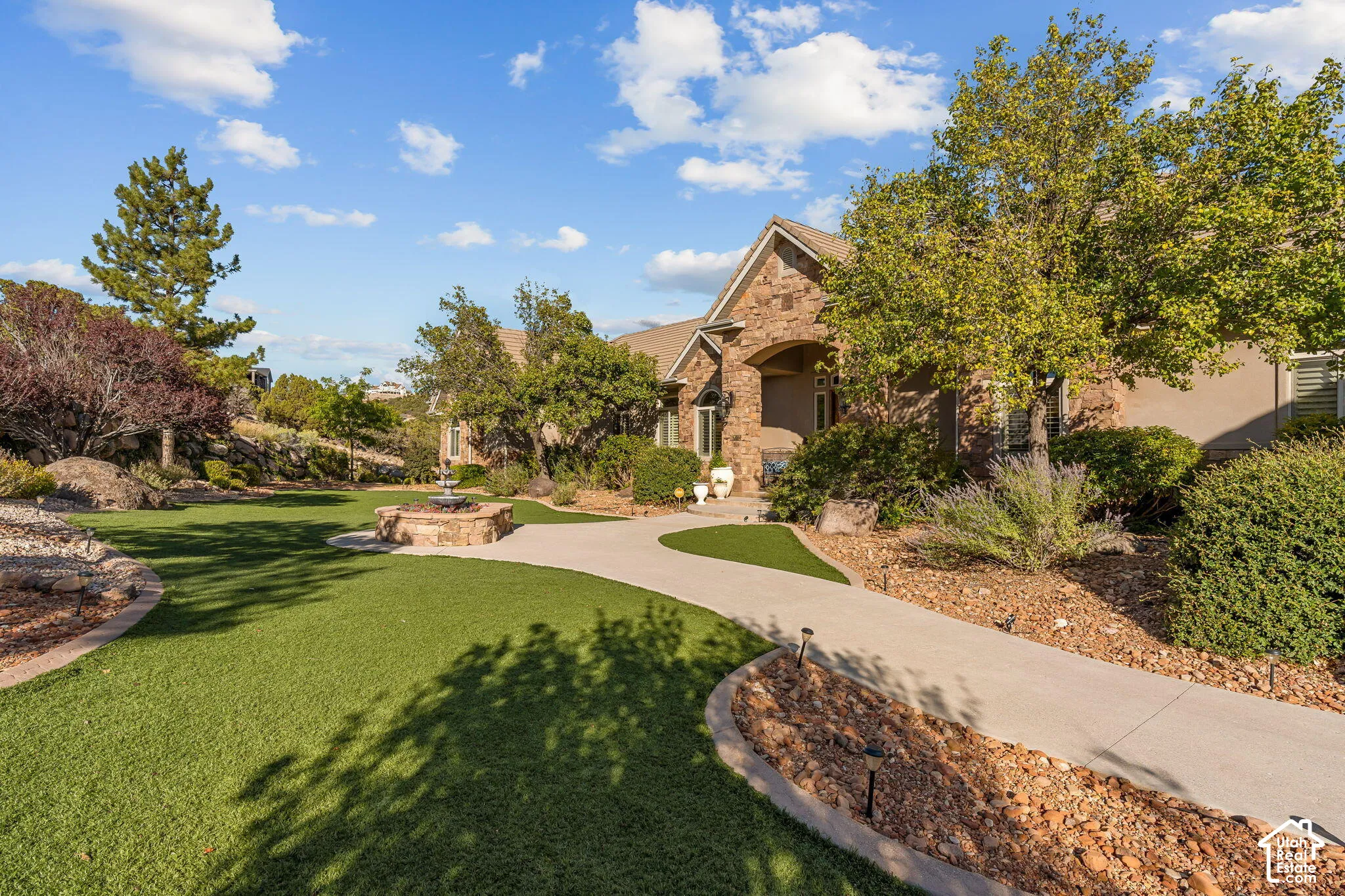 Stone and stucco exterior, arched entry, paved walkways, artificial turf lawn, and a stone-built water feature