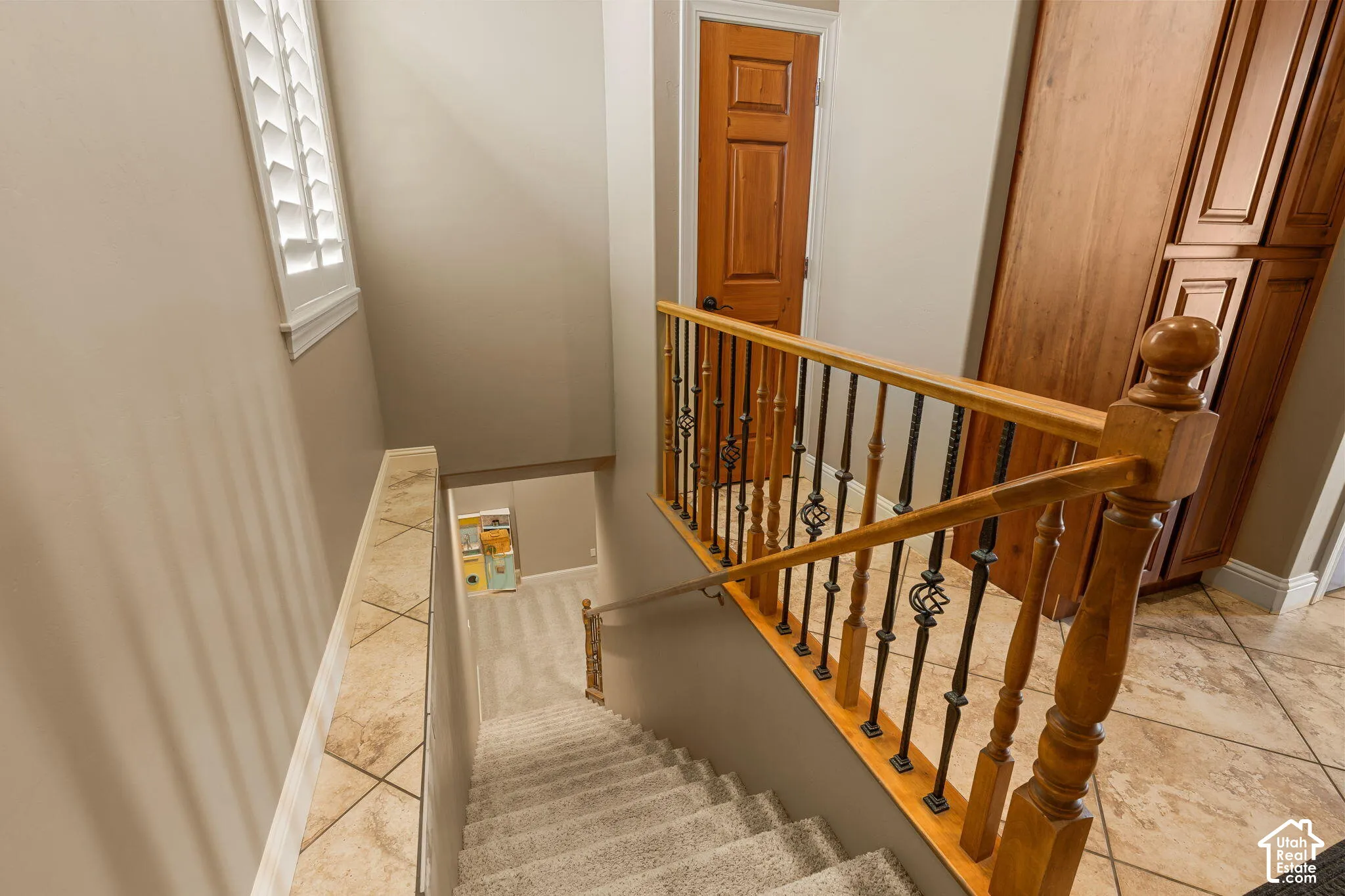 Staircase with wood handrails, wrought iron balusters, and carpeted treads