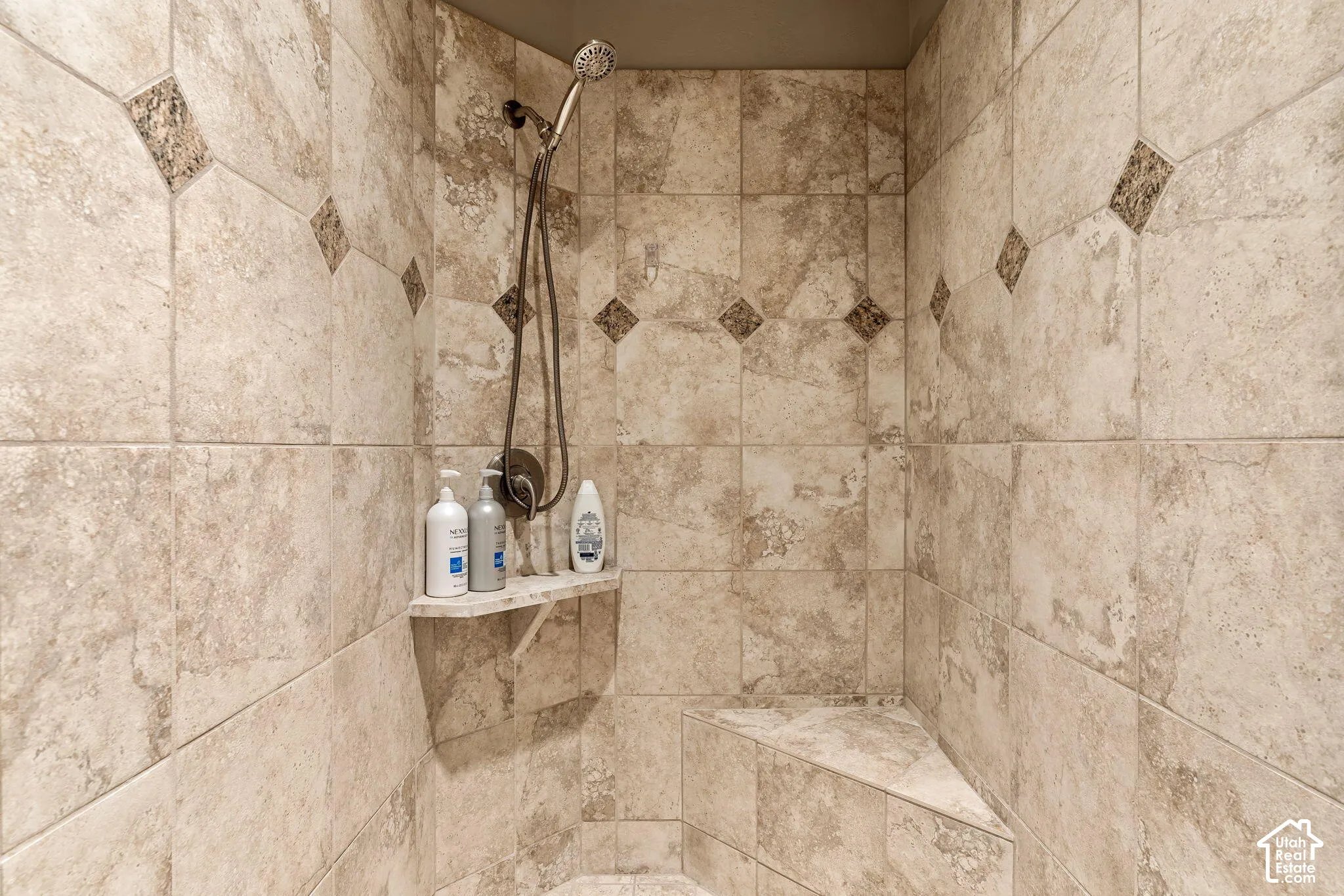Tiled shower enclosure featuring a corner bench and a built-in shelf