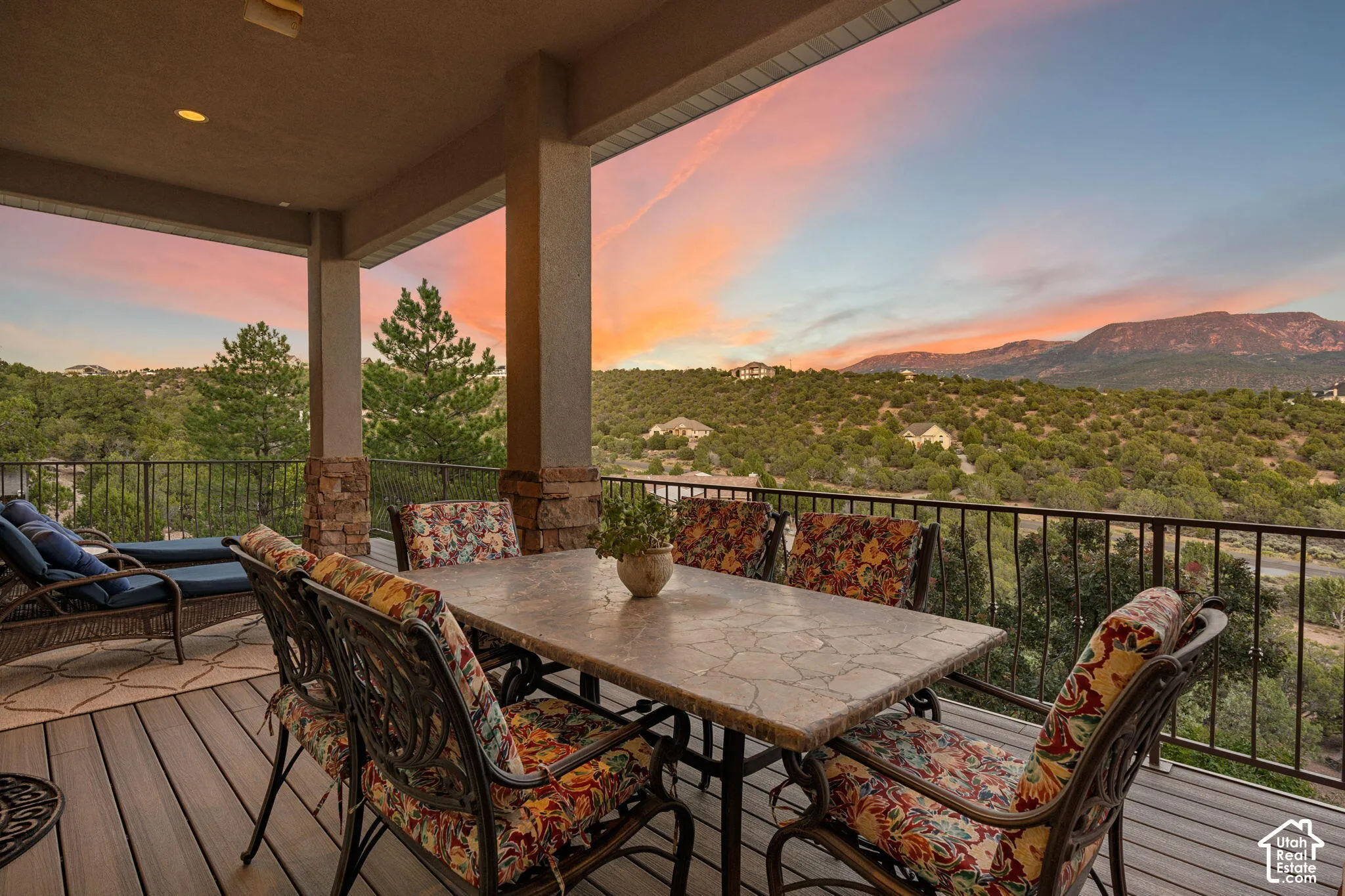 Covered outdoor patio with composite decking and a black metal railing, featuring stone-clad pillars and a distant mountain landscape