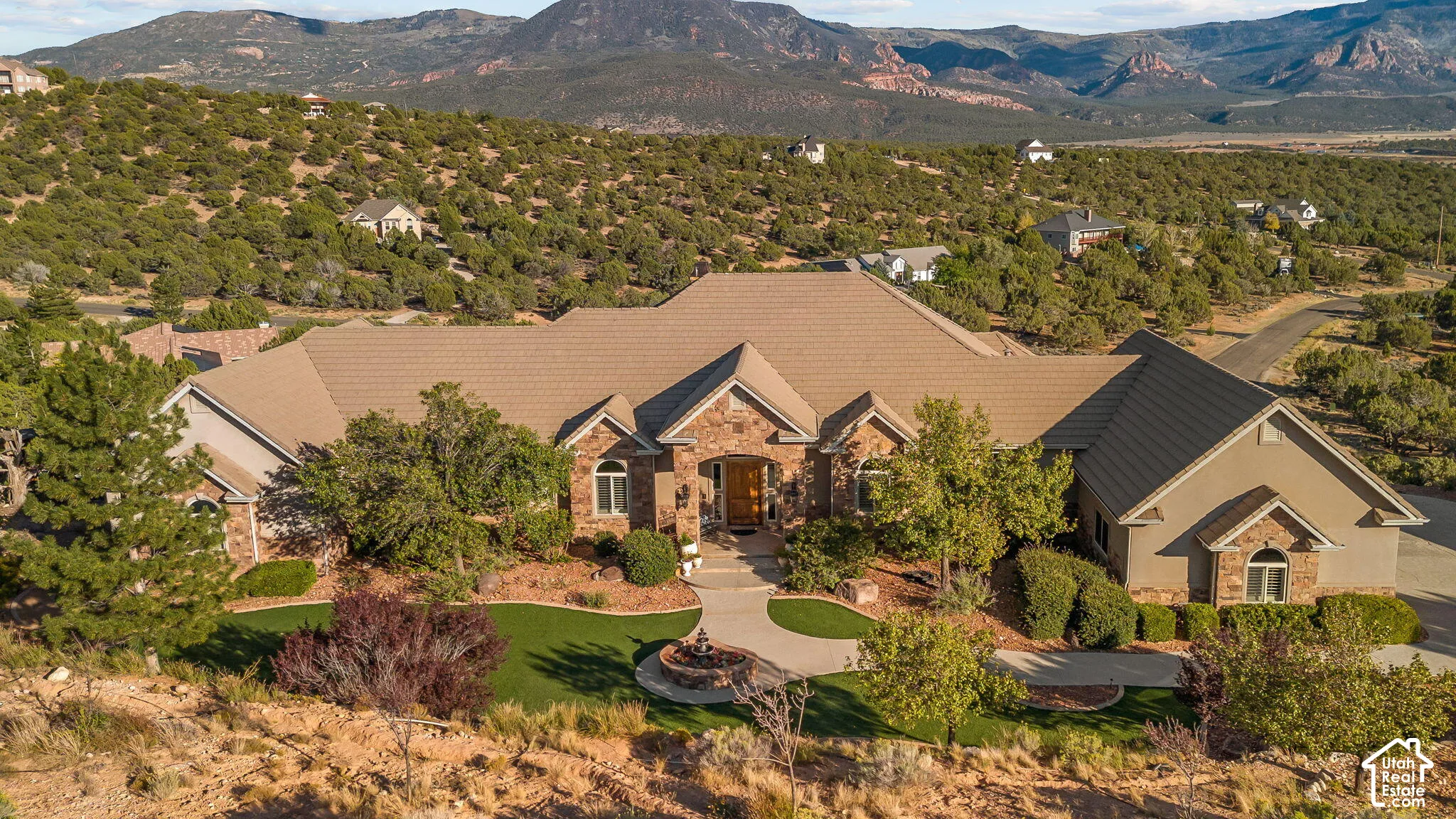 Stone and stucco exterior, multi-pitch roof, manicured front lawn, paved driveway, and established landscaping