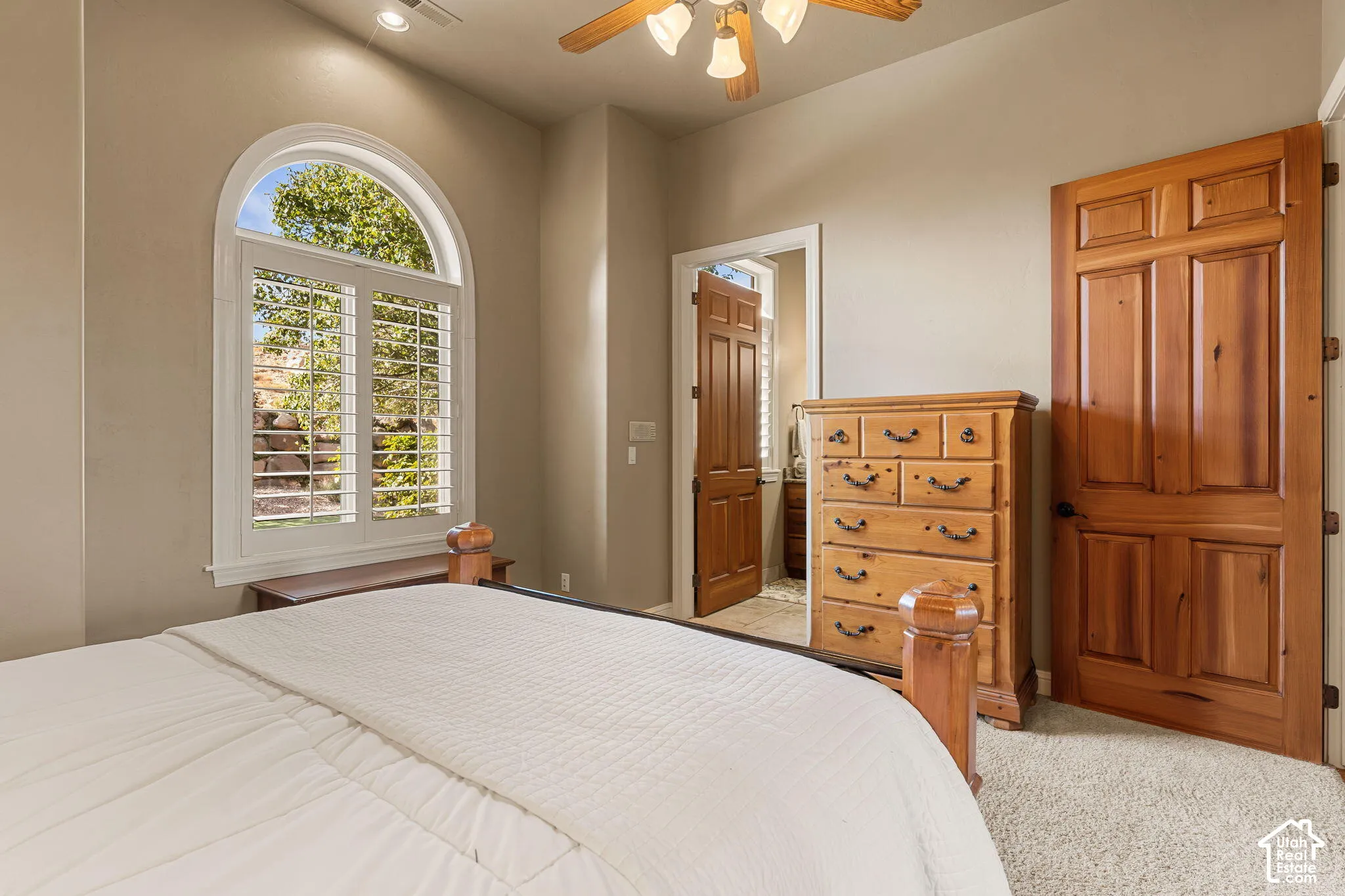 Arched window with plantation shutters, wood-paneled doors, textured carpeting, and a ceiling fan with integrated lighting