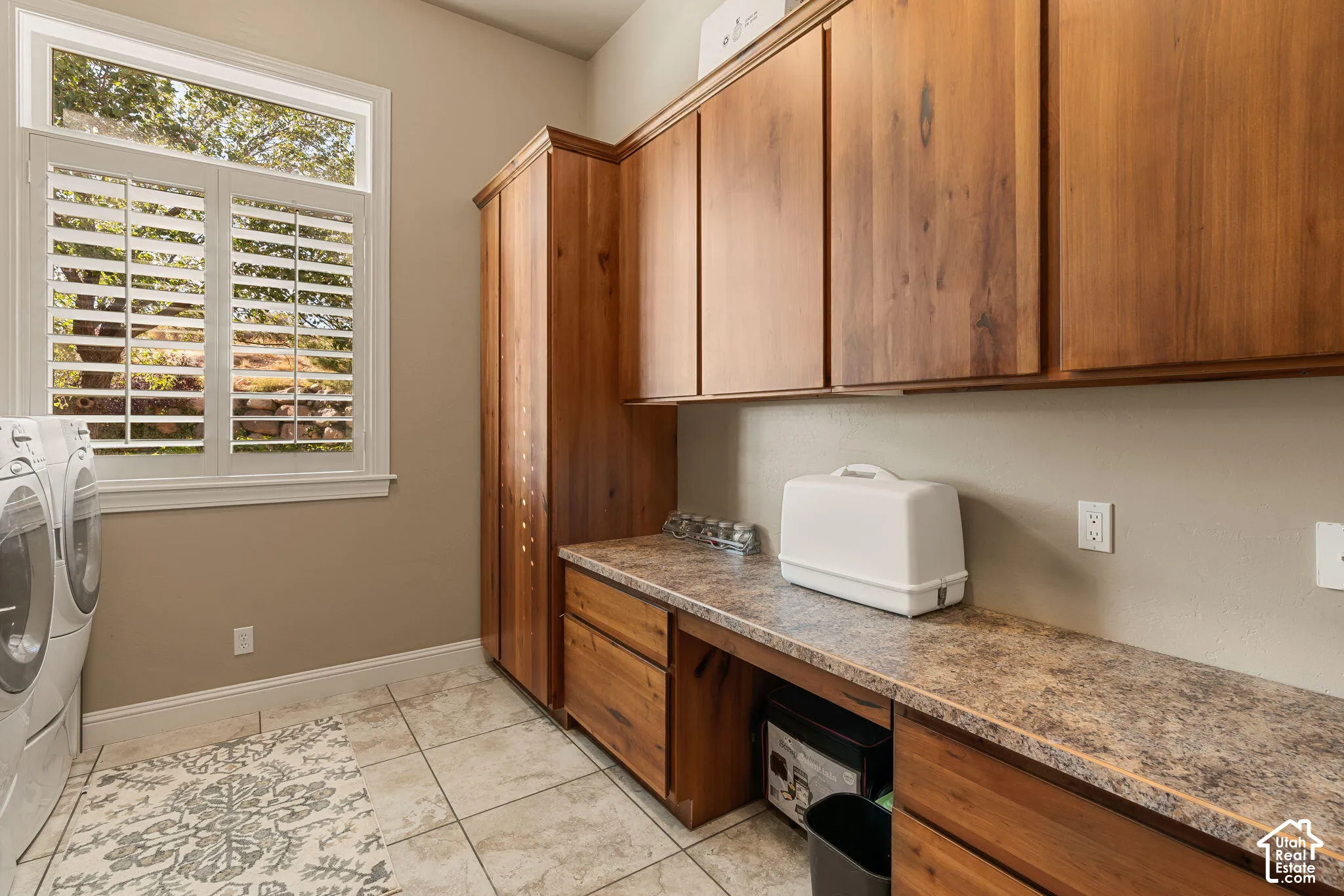 Utility room featuring wood-finish cabinetry, tile flooring, and a window with plantation shutters