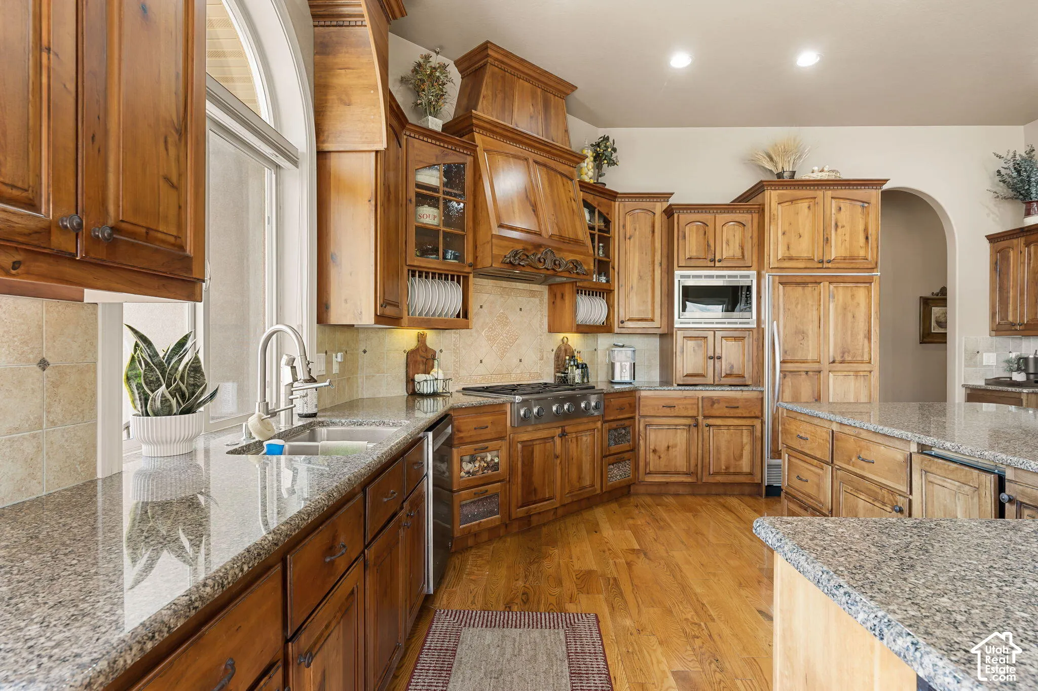 Hardwood flooring, light-toned granite countertops, wood cabinetry, stainless steel appliances, and an arched window