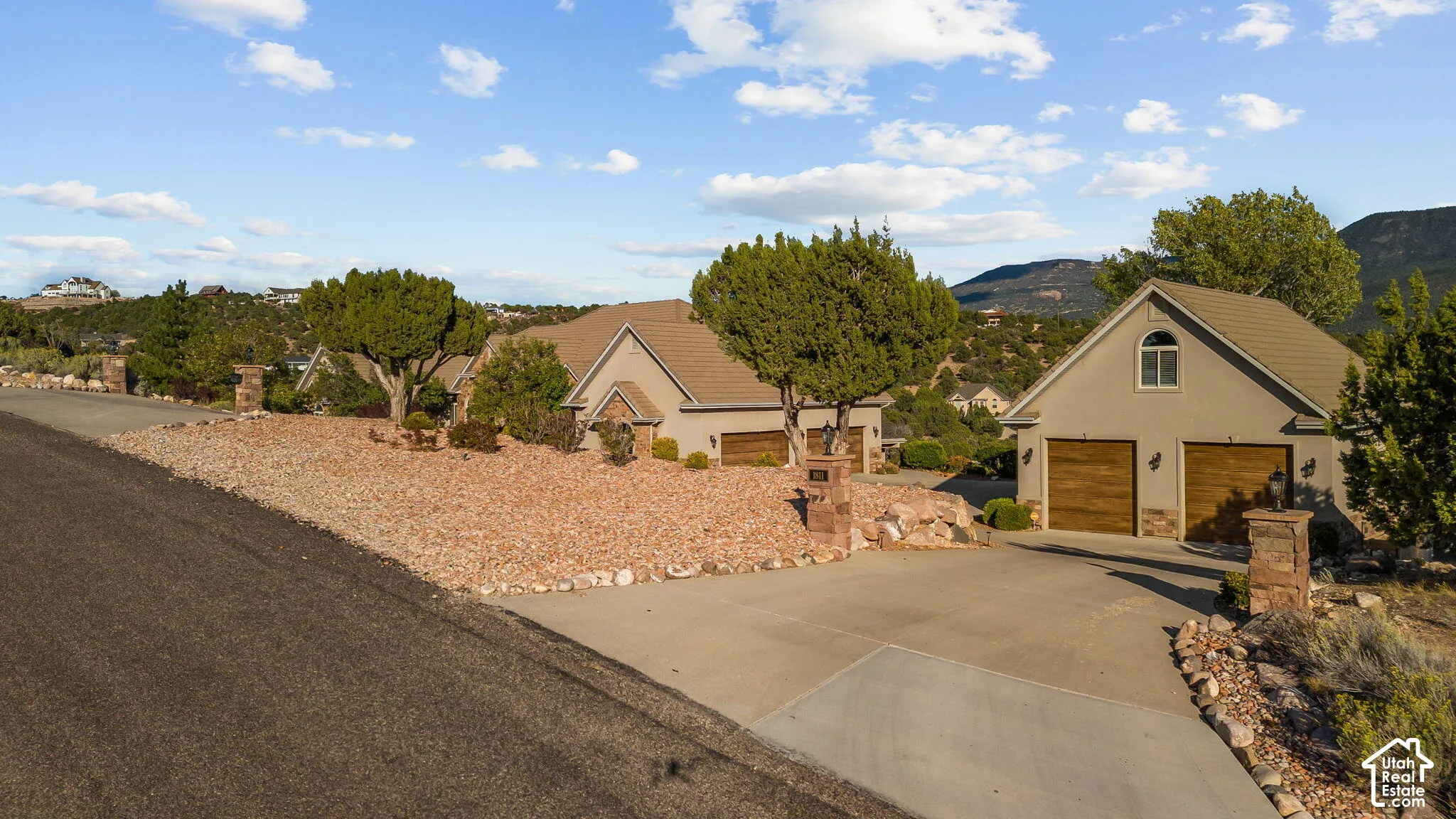 Two stucco homes with composite shingle roofs and integrated two-car garages, mature landscaping with natural rock and shrubs, and a concrete driveway
