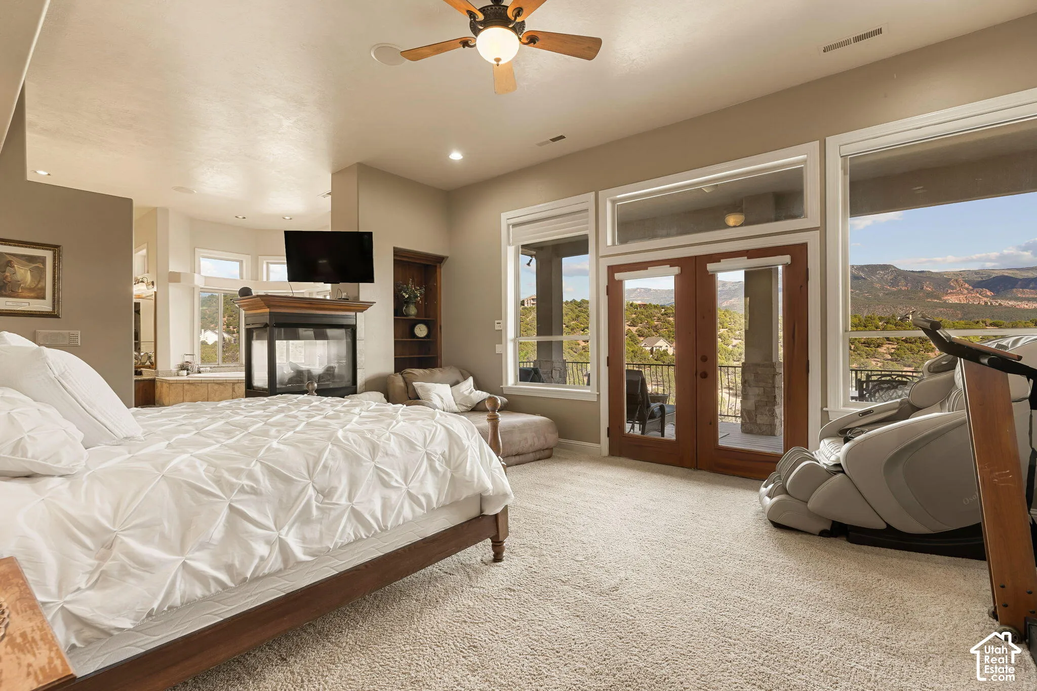 Dual-sided fireplace with wood mantel, ceiling fan with integrated lighting, wall-mounted television, built-in shelving, and direct exterior access through French doors