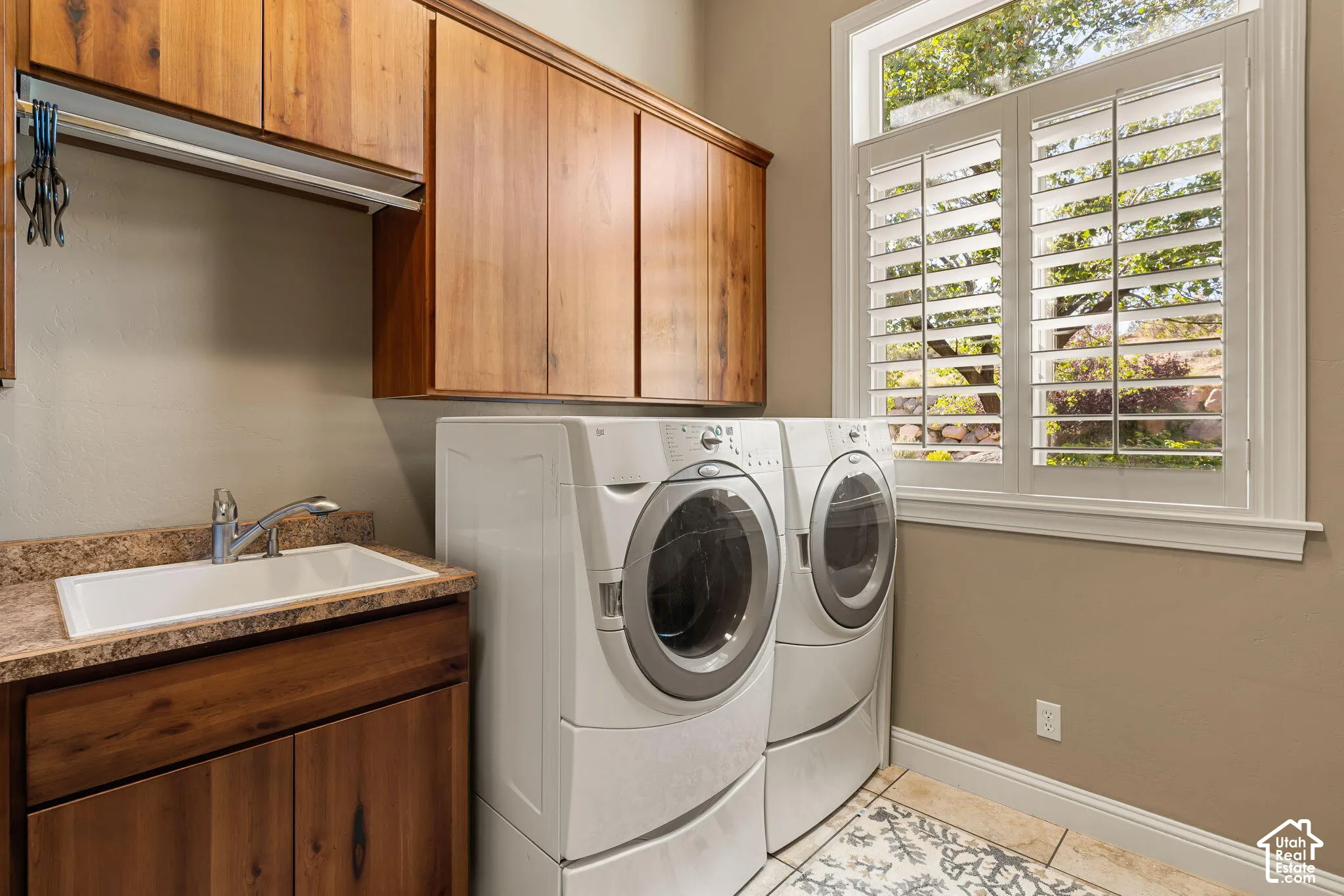 Laundry room featuring wood-finish cabinetry, a utility sink, and built-in window shutters