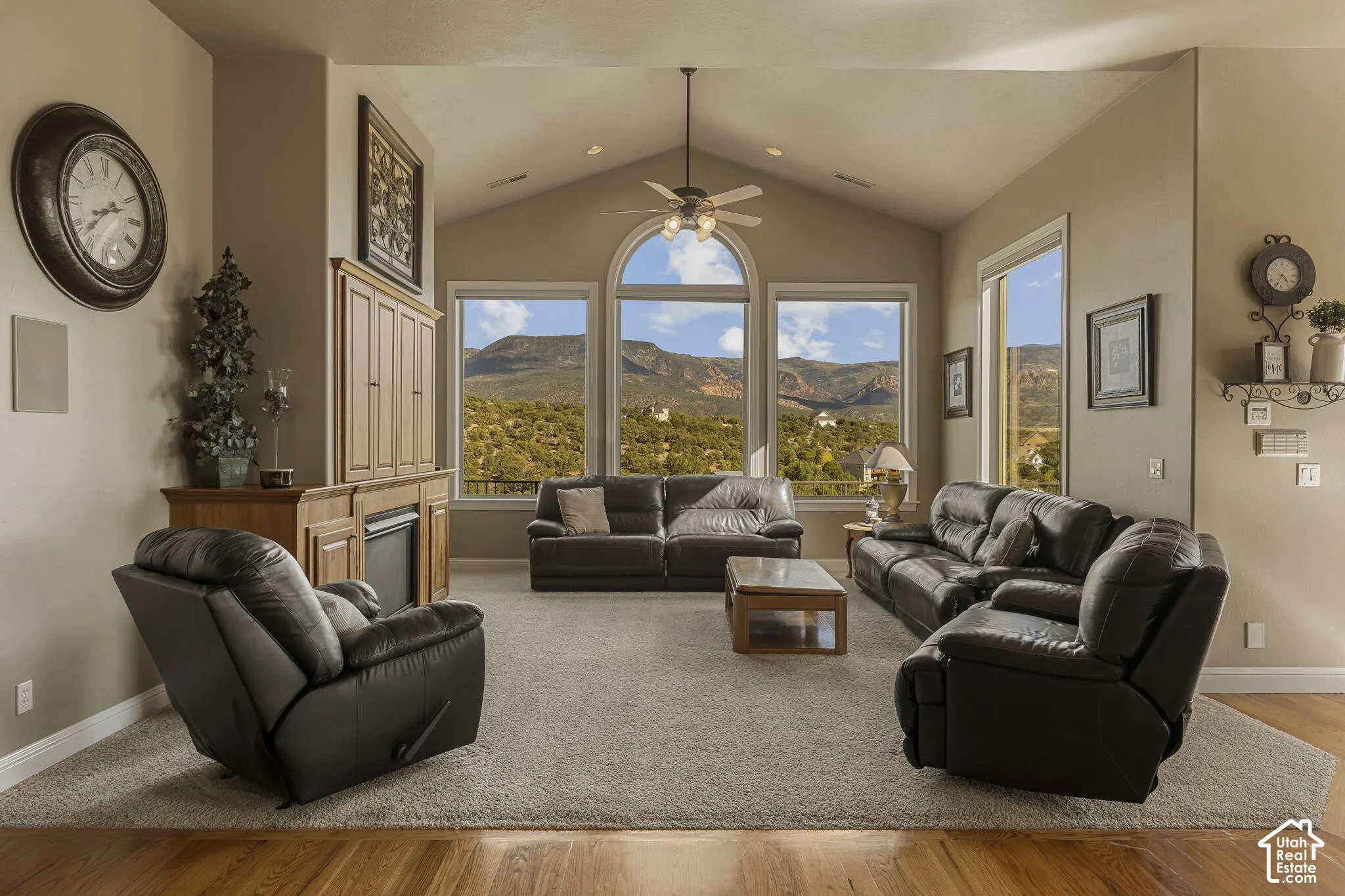 Vaulted ceiling with a ceiling fan, broad windows offering a mountain backdrop, built-in cabinetry, and wood-finish flooring