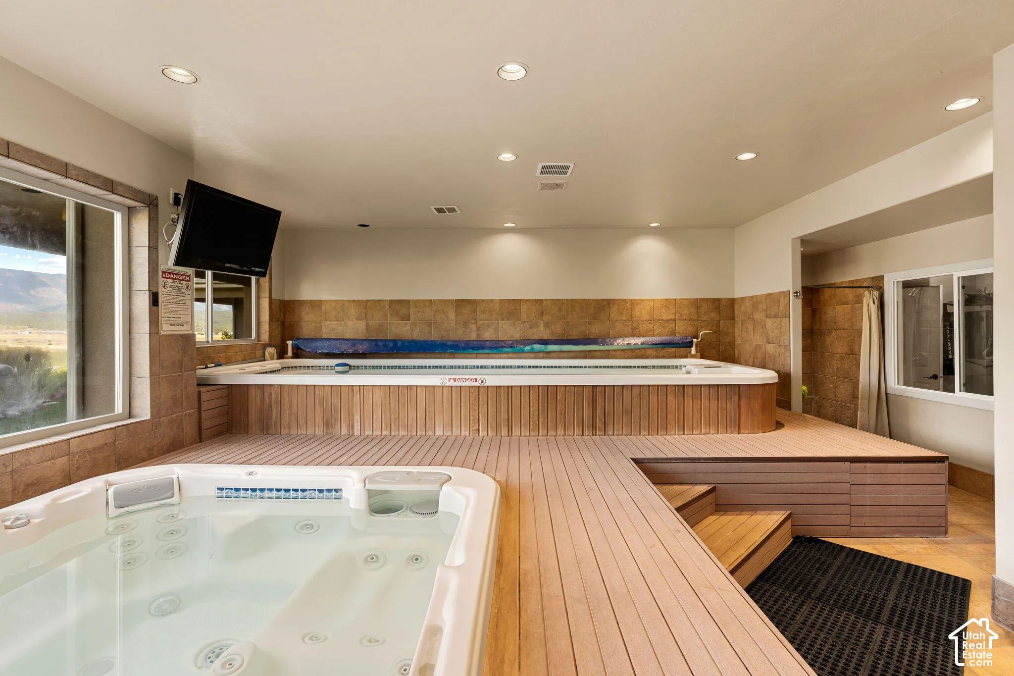 Indoor spa room featuring a built-in hot tub, a swim spa, a wood-finish deck, tile wainscoting, and recessed lighting