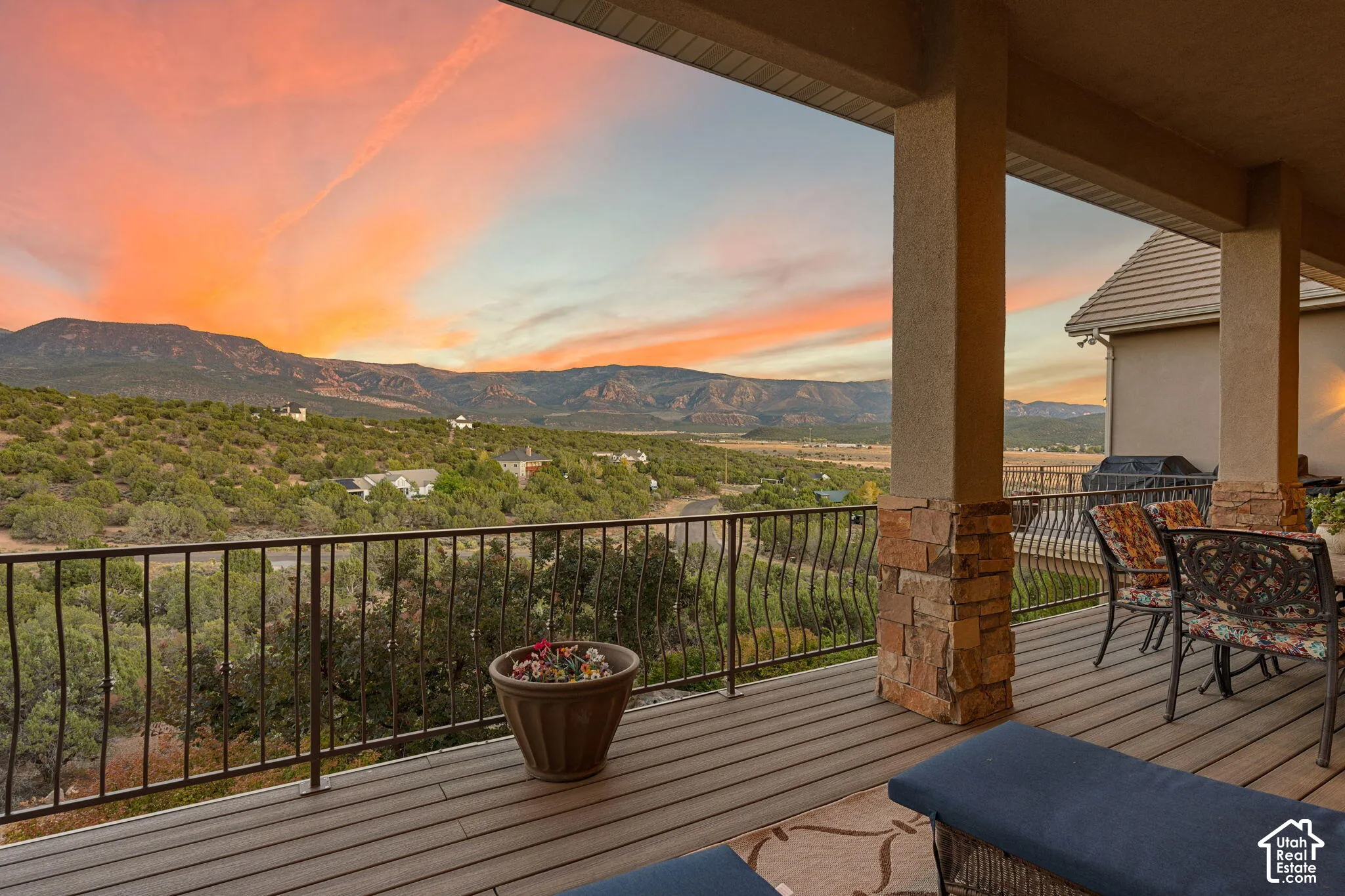 Expansive covered deck featuring composite decking, stone-clad columns, and a wrought iron railing, with a mountainous backdrop
