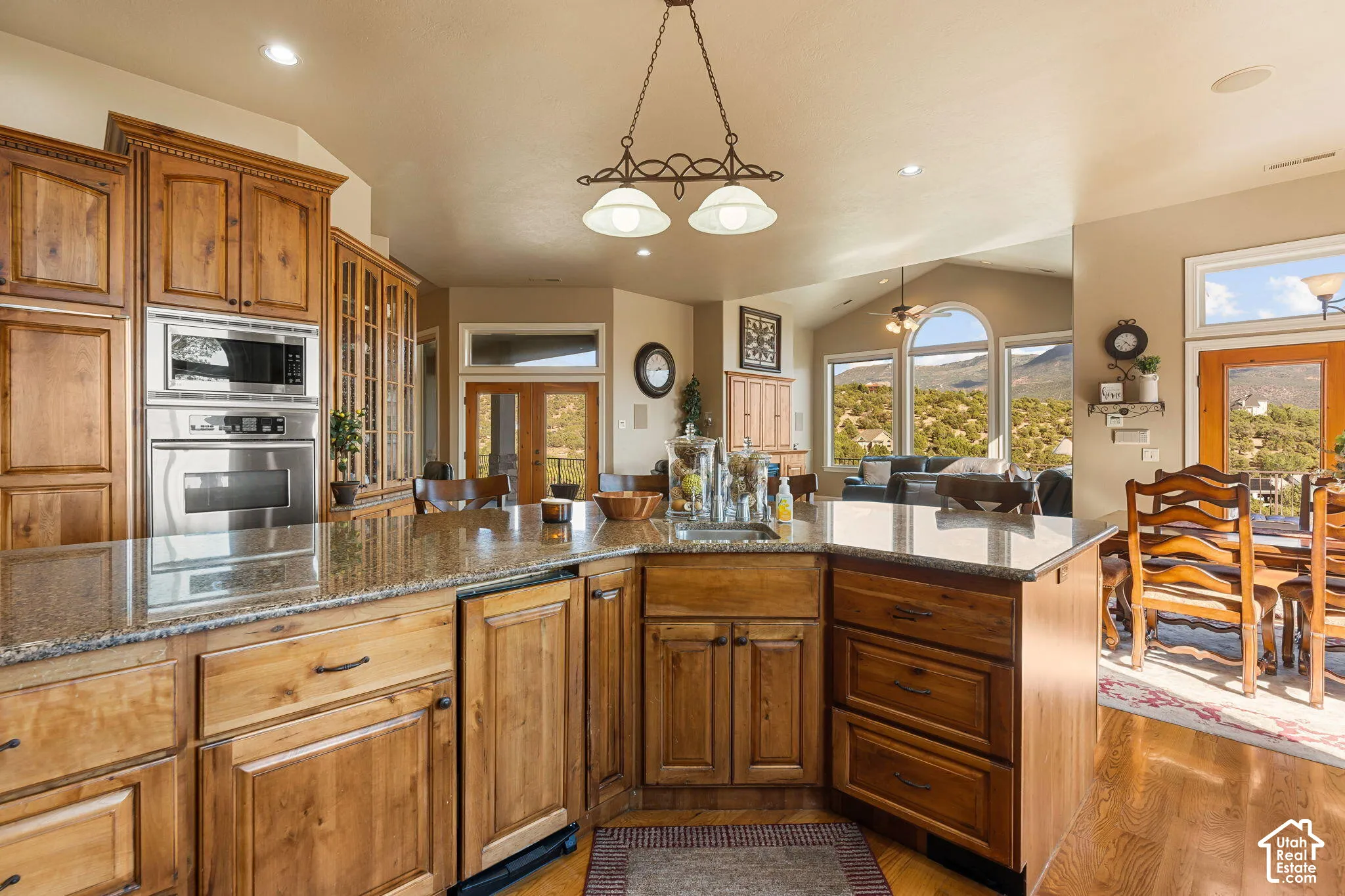 Kitchen featuring light wood cabinetry, stone-finish countertops, stainless steel built-in appliances, and a central island with a sink