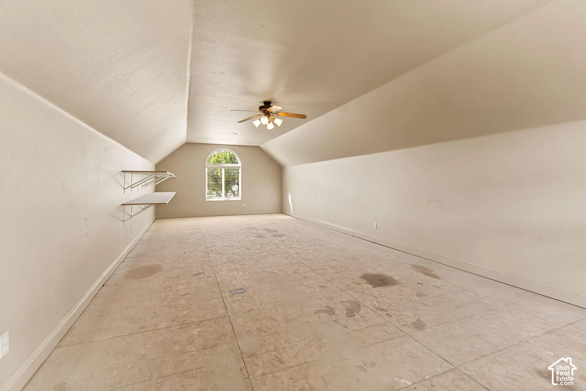 Arched window, vaulted ceiling, ceiling fan, wall-mounted shelving, and wood subflooring