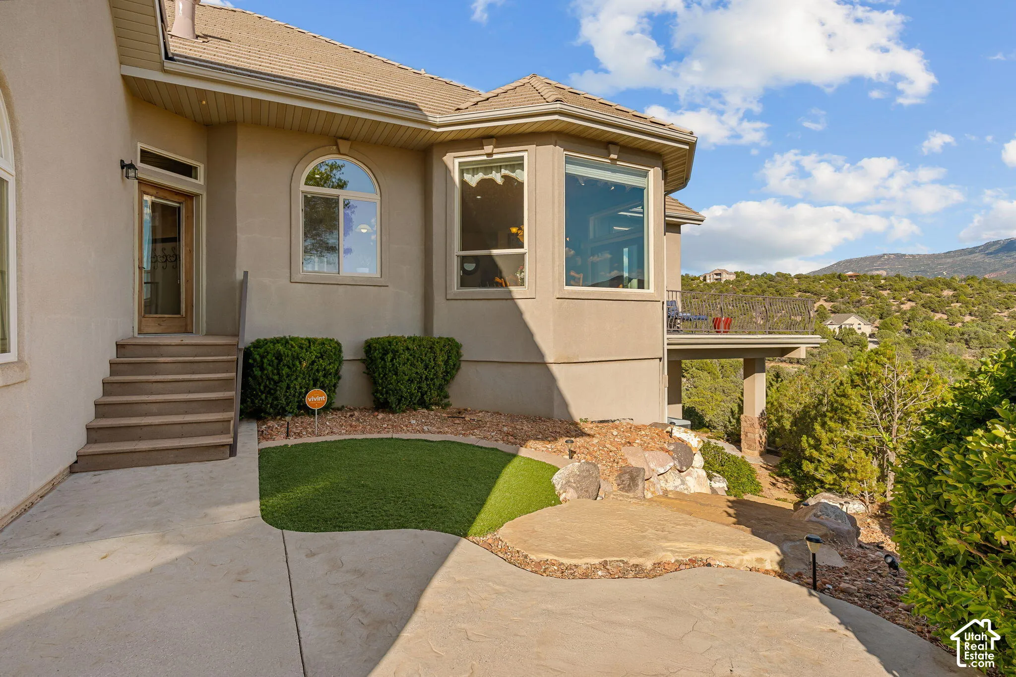 Exterior featuring a stucco finish, multi-pane windows, a recessed entry, a covered patio, and a terraced landscape with natural rock elements