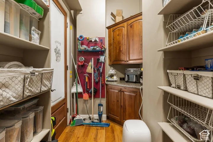 Built-in shelving, wood-finish flooring, pegboard wall organization, wood cabinetry, and granite-look countertop