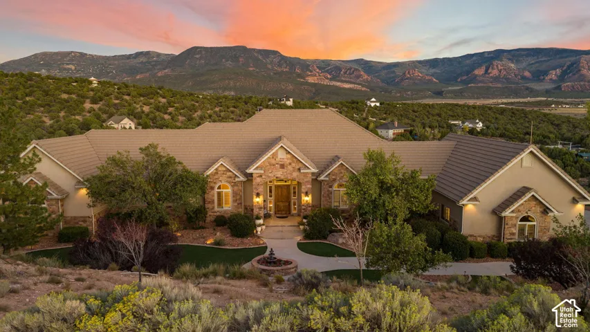 Stucco and stone exterior with arched windows, mature landscaping, and a paver driveway