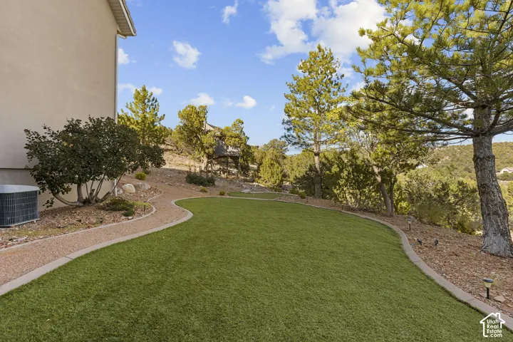 Landscaped yard featuring a manicured artificial turf lawn, a gravel pathway with concrete edging, and mature trees