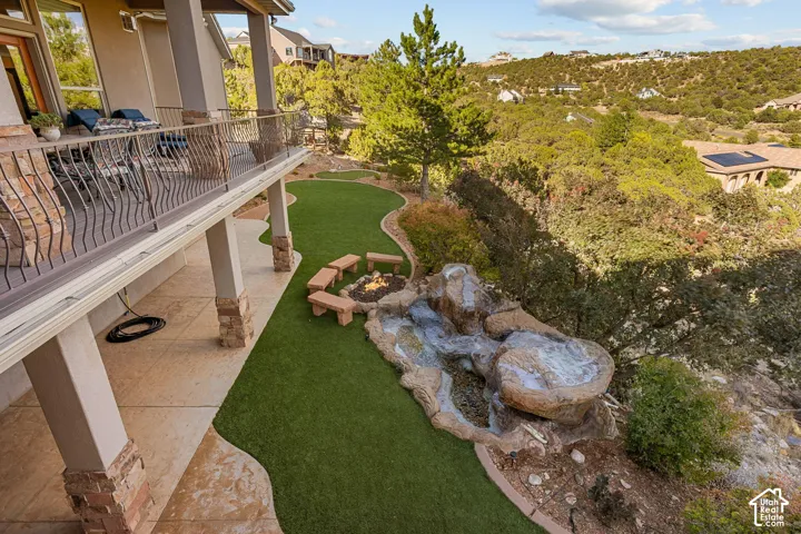 Expansive outdoor living area featuring a covered patio, wrought iron railing, artificial turf lawn, and a custom rock water feature