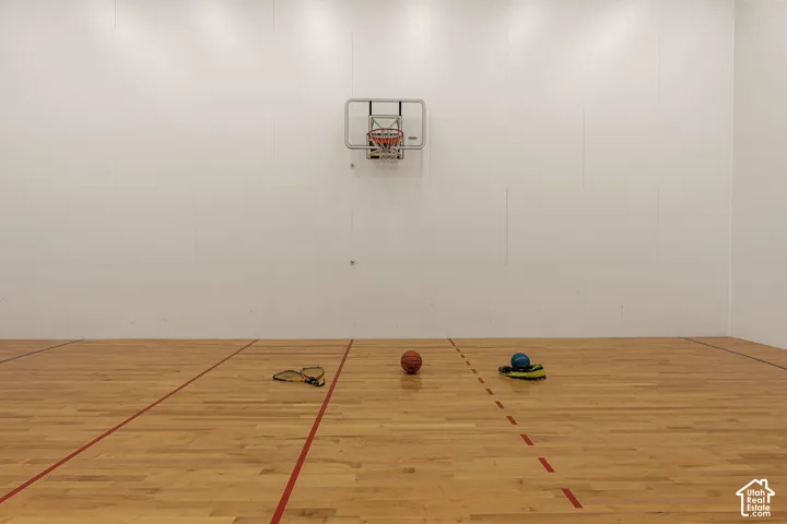 Indoor athletic court with light wood-finish flooring, white walls, and an attached basketball hoop