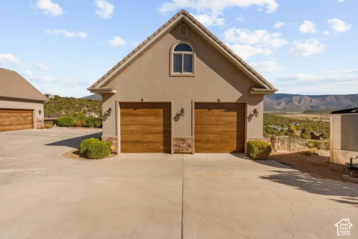 Two-car garage with wood-finish doors and stone accents, featuring an arched window and exterior sconces, situated on a paved driveway with distant mountain scenery