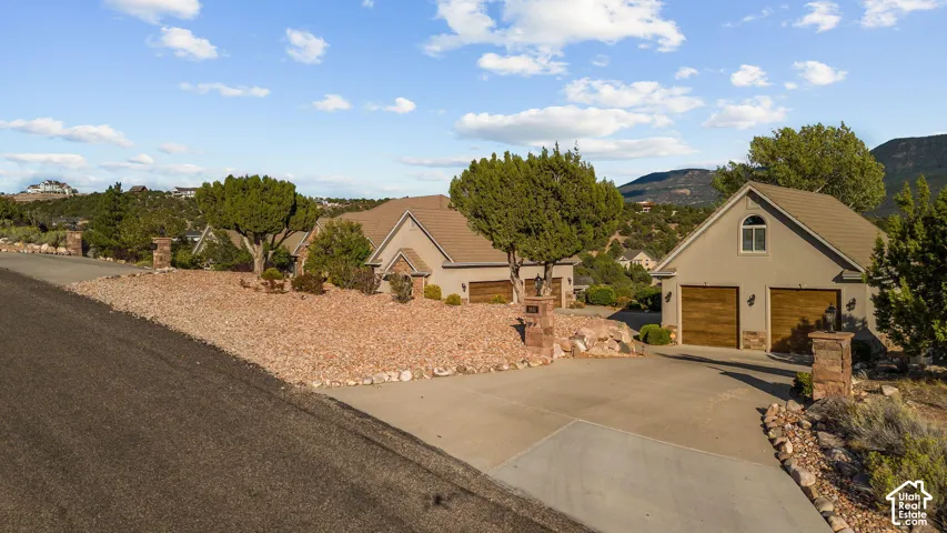 Two stucco homes with composite shingle roofs and integrated two-car garages, mature landscaping with natural rock and shrubs, and a concrete driveway