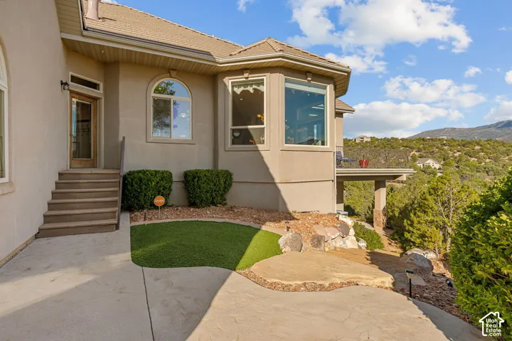 Exterior featuring a stucco finish, multi-pane windows, a recessed entry, a covered patio, and a terraced landscape with natural rock elements