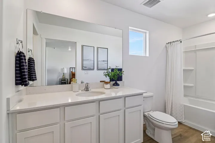 White vanity with a single basin sink, light-colored countertop, large wall-mounted mirror, and wood-finish flooring
