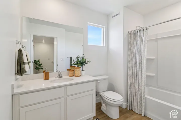 White vanity with a quartz countertop and integrated sink, a rectangular mirror, a window providing natural illumination, wood-finish flooring, and a white tub with an integrated shower