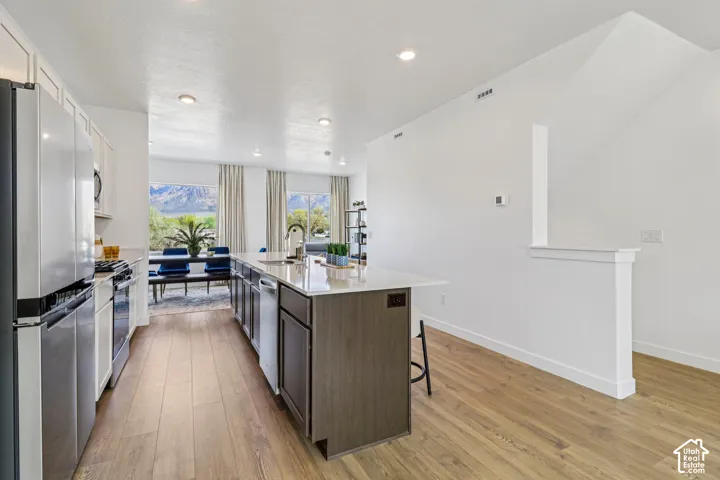 Kitchen featuring stainless steel appliances, a large island with a sink, wood-finish flooring, and recessed lighting