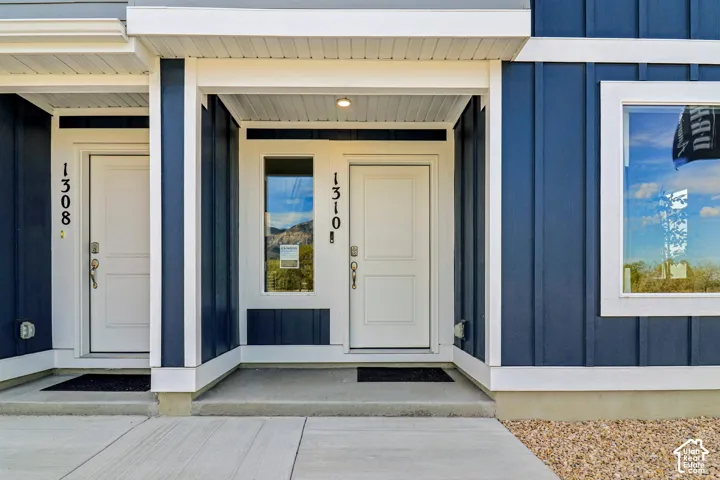 Board and batten siding in a deep blue hue, crisp white trim, a recessed entry with a paneled door, a sidelight, and an exterior light fixture