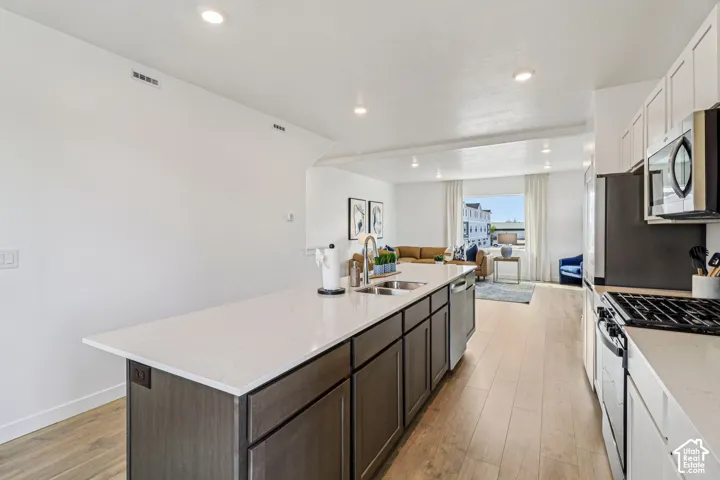 Kitchen featuring a large island with a double basin sink, stainless steel appliances, wood-finish flooring, and recessed lighting
